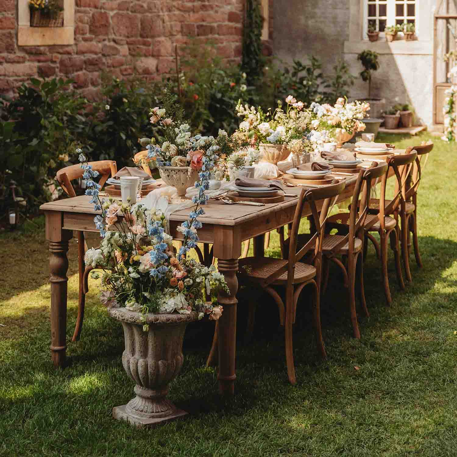 Mesa de jardín de madera con decoración floral y vajilla sobre césped soleado