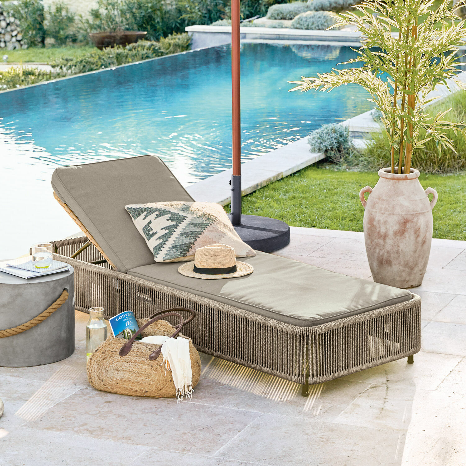 Tumbona de jardín beige con cojín y estructura trenzada junto a la piscina, ambiente veraniego