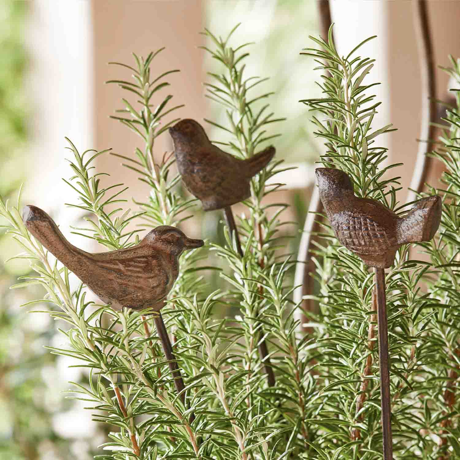 Pájaros decorativos de metal marrón en varillas entre ramas verdes de romero