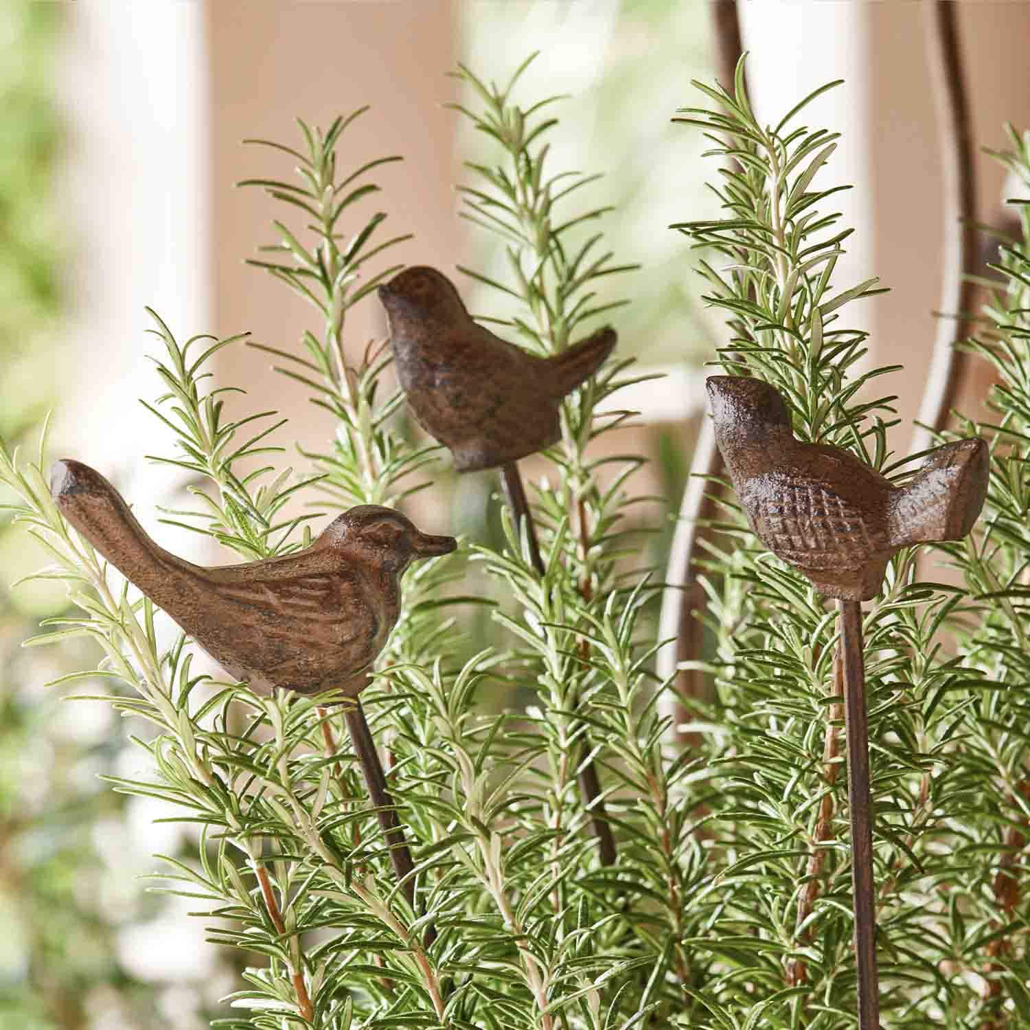Pájaros decorativos de metal marrón en varillas entre ramas verdes de romero