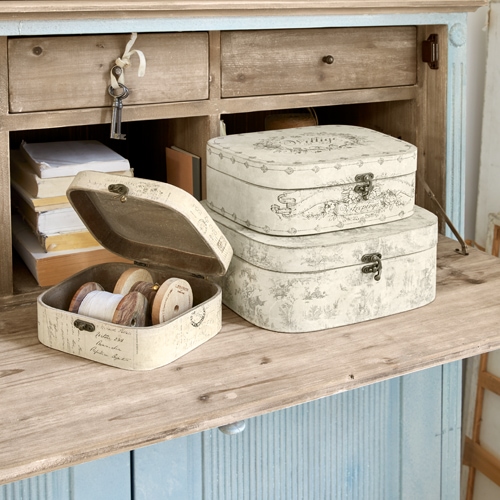 Conjunto de tres cajas decorativas crema con diseño vintage sobre mesa de madera, almacenamiento práctico
