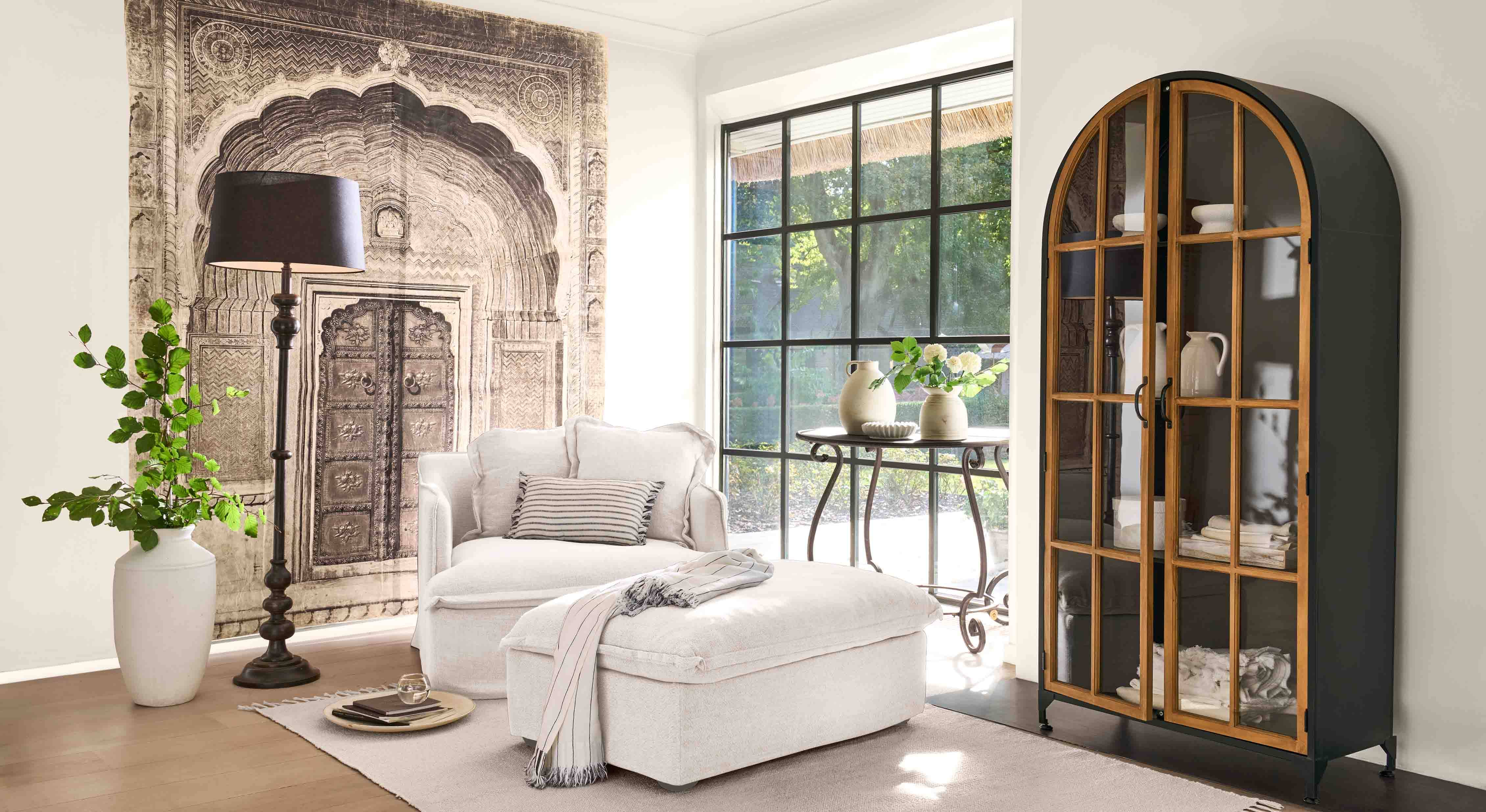 Sillón blanco cómodo con reposapiés y lámpara negra en salón luminoso con vitrina decorativa