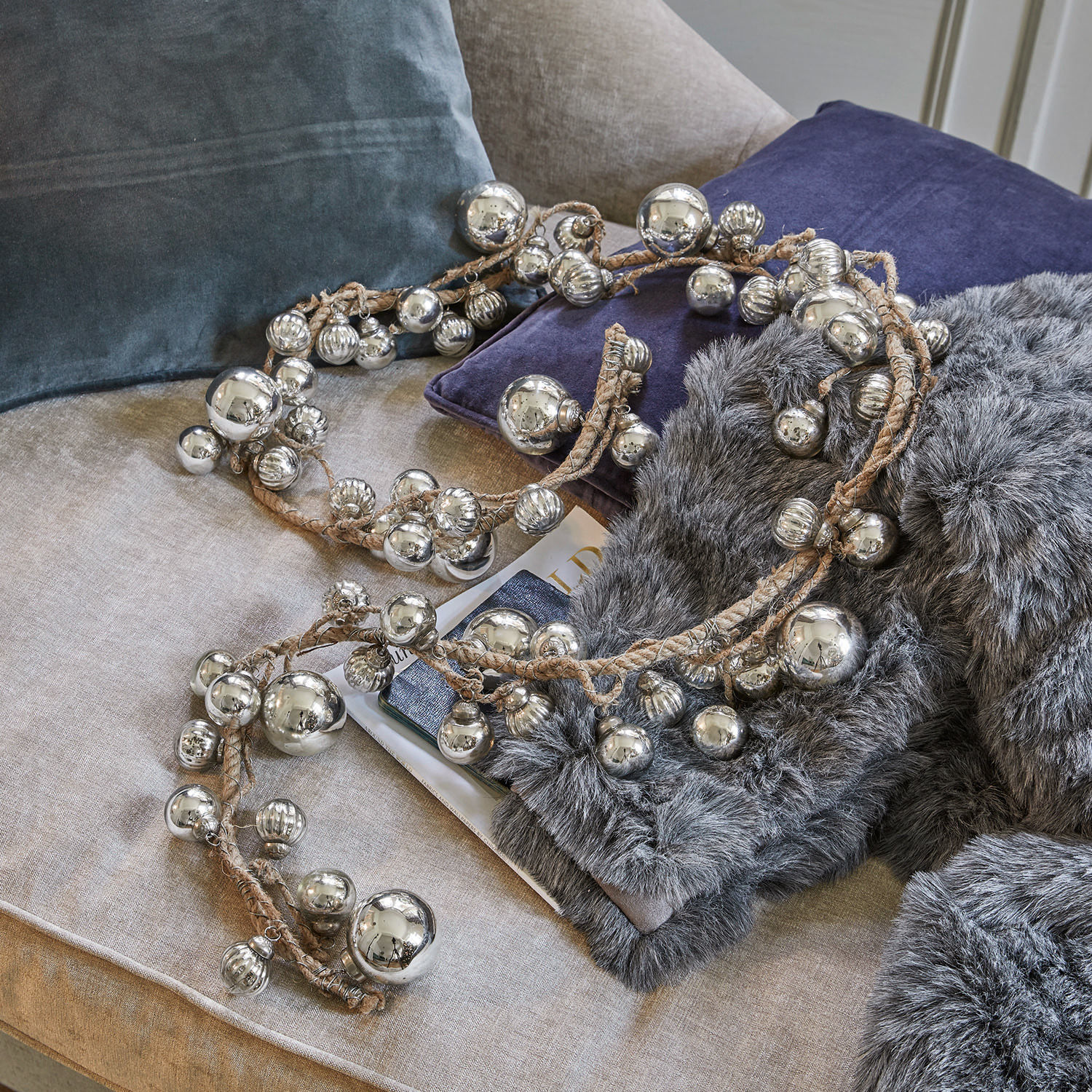 Guirnalda Pearls Guirnalda decorativa con bolas metálicas plateadas en cuerda de lino sobre sofá con cojines