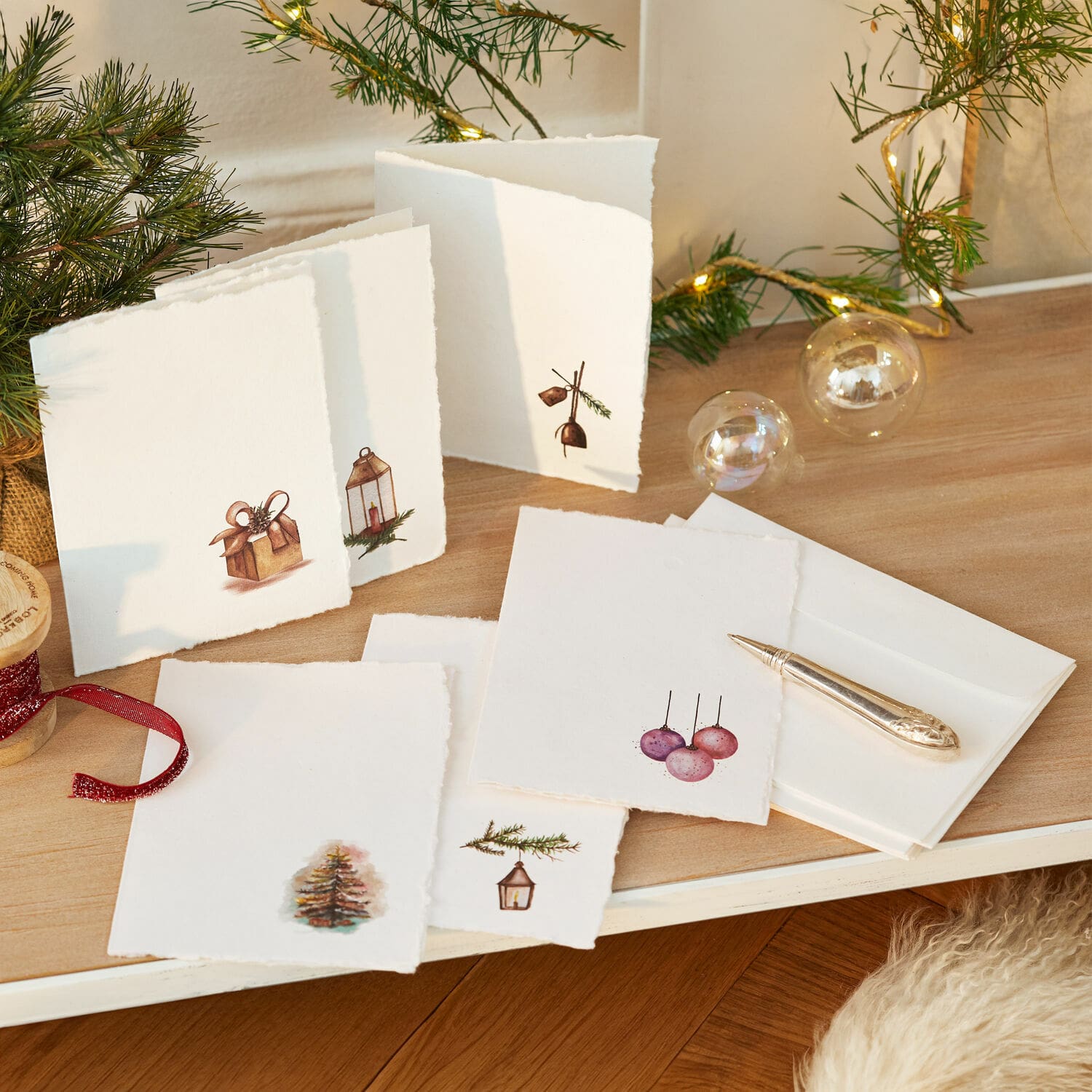 Set de 6 tarjetas de felicitación Aeloria Conjunto de tarjetas navideñas blancas con motivos de árbol y regalos sobre mesa de madera con luces LED