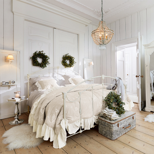 Dormitorio acogedor con cama metálica blanca, ropa de cama beige, decoración en paredes y suelo de madera clara
