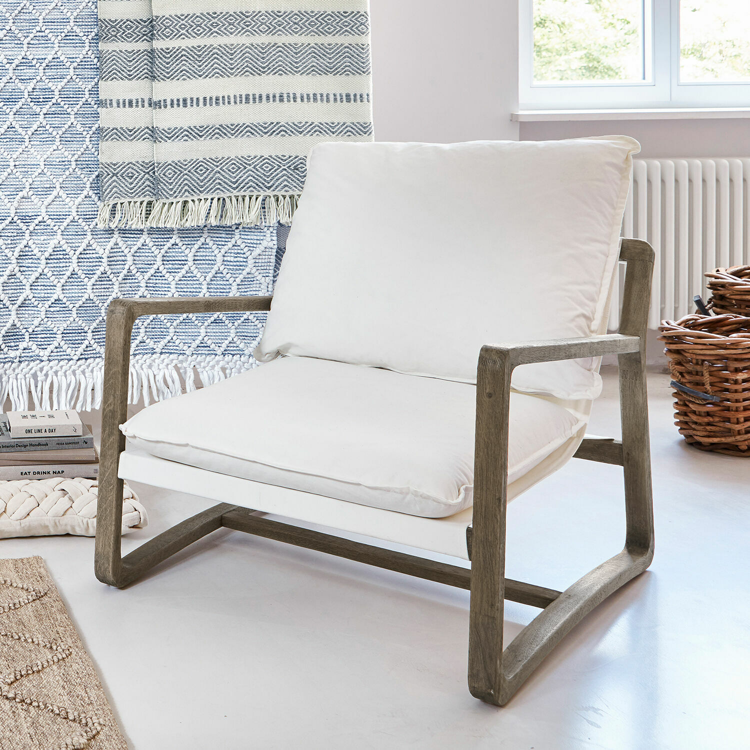 Sillón con estructura de madera y cojín blanco de algodón en interior moderno y luminoso