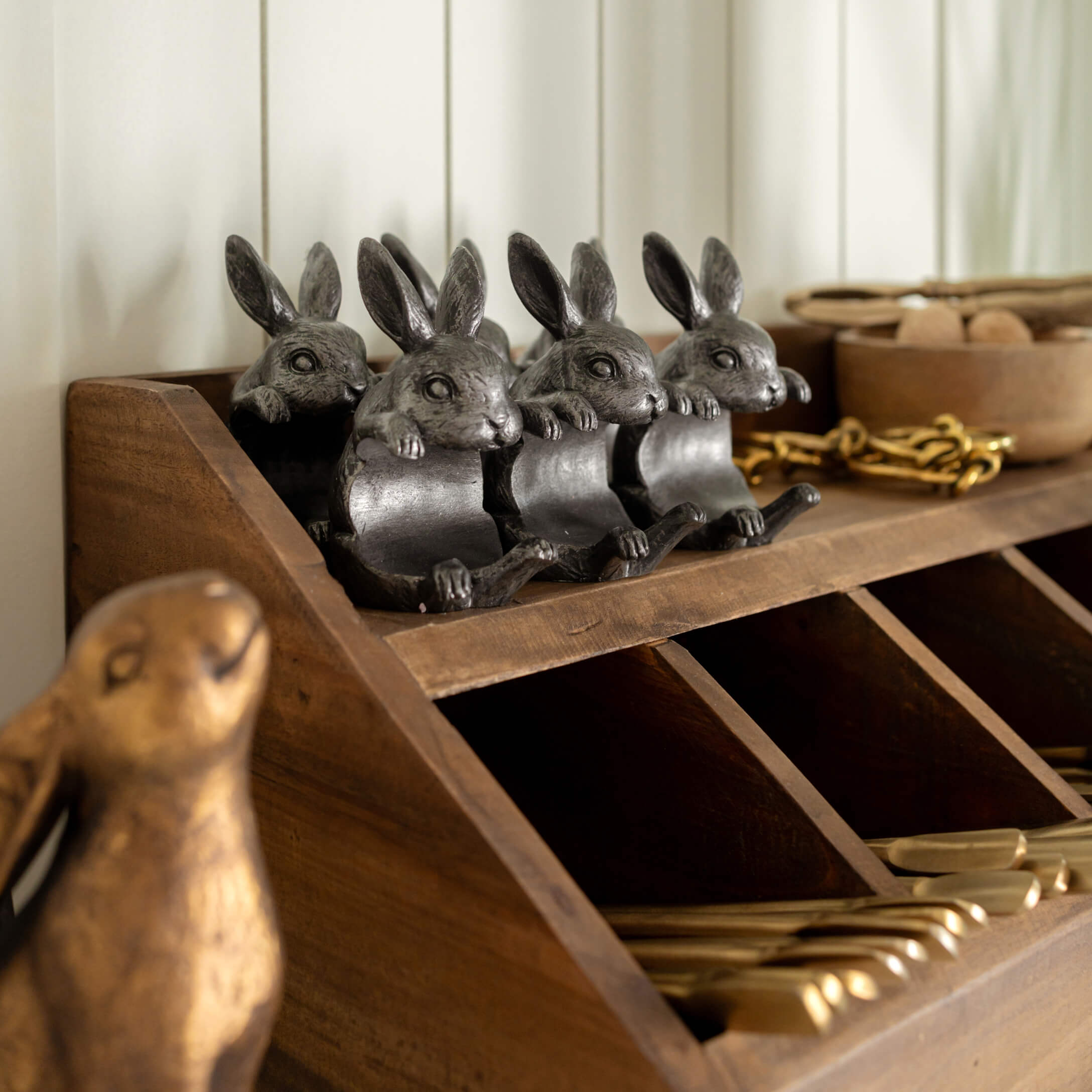 Cuatro decoraciones de conejos de metal gris oscuro sobre una estantería de madera con compartimentos