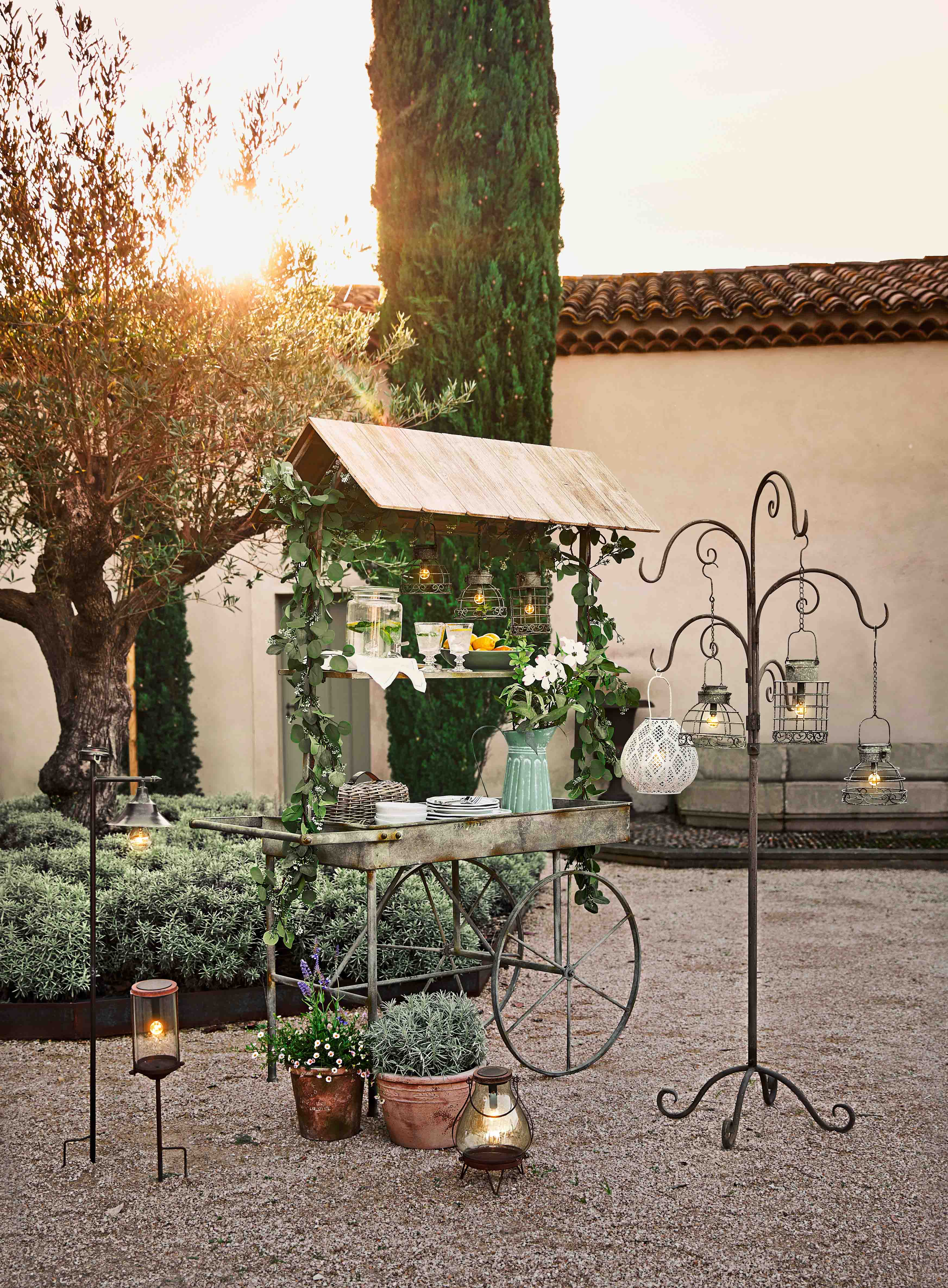 Carro de jardín de metal con techo de madera, decoraciones vegetales y faroles colgantes en exterior