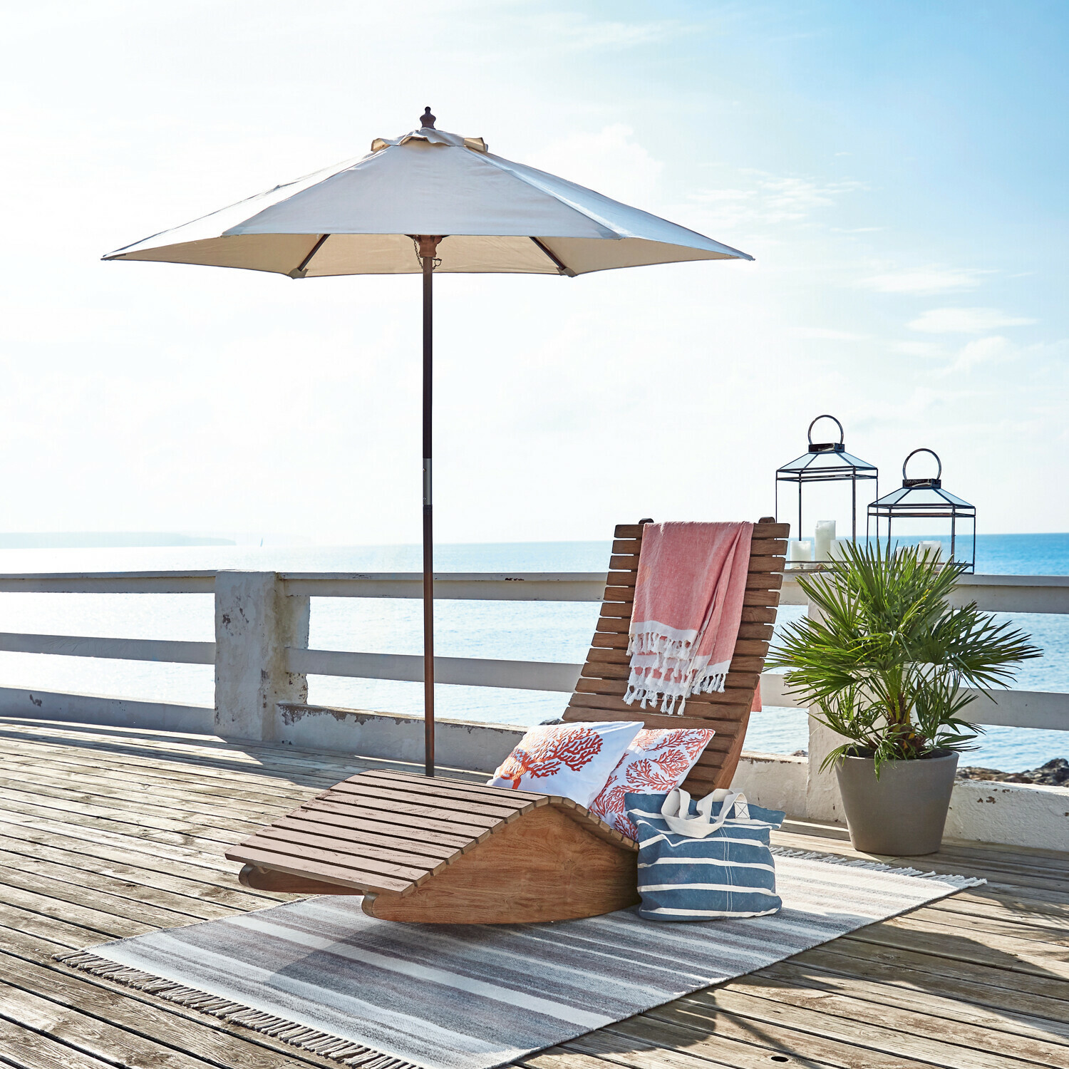 Sombrilla Enfield Tumbona de madera con sombrilla blanca y cojines decorativos en terraza junto al mar para descanso