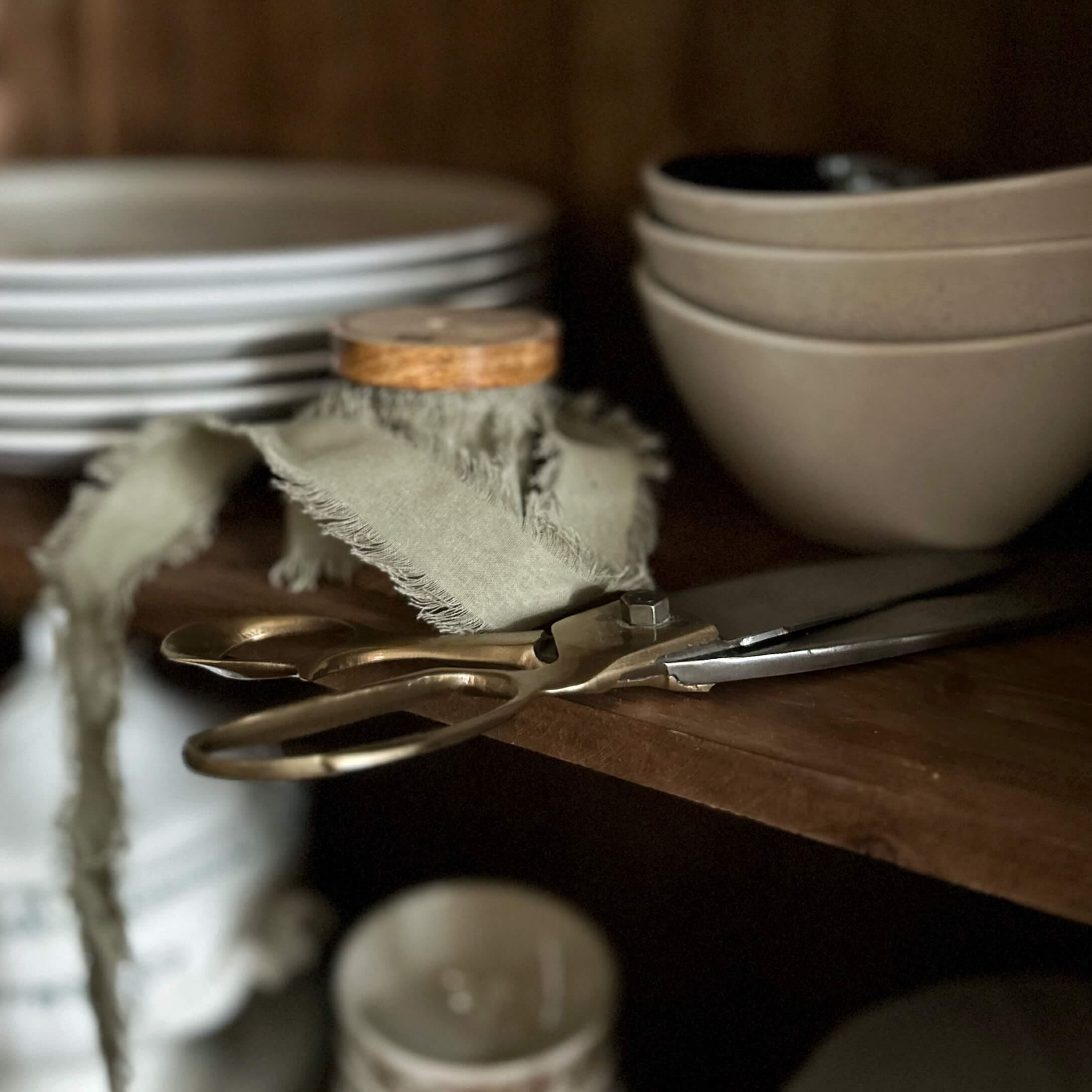 Tijeras antiguas de latón sobre estante de madera junto a cuencos y platos beige en cocina