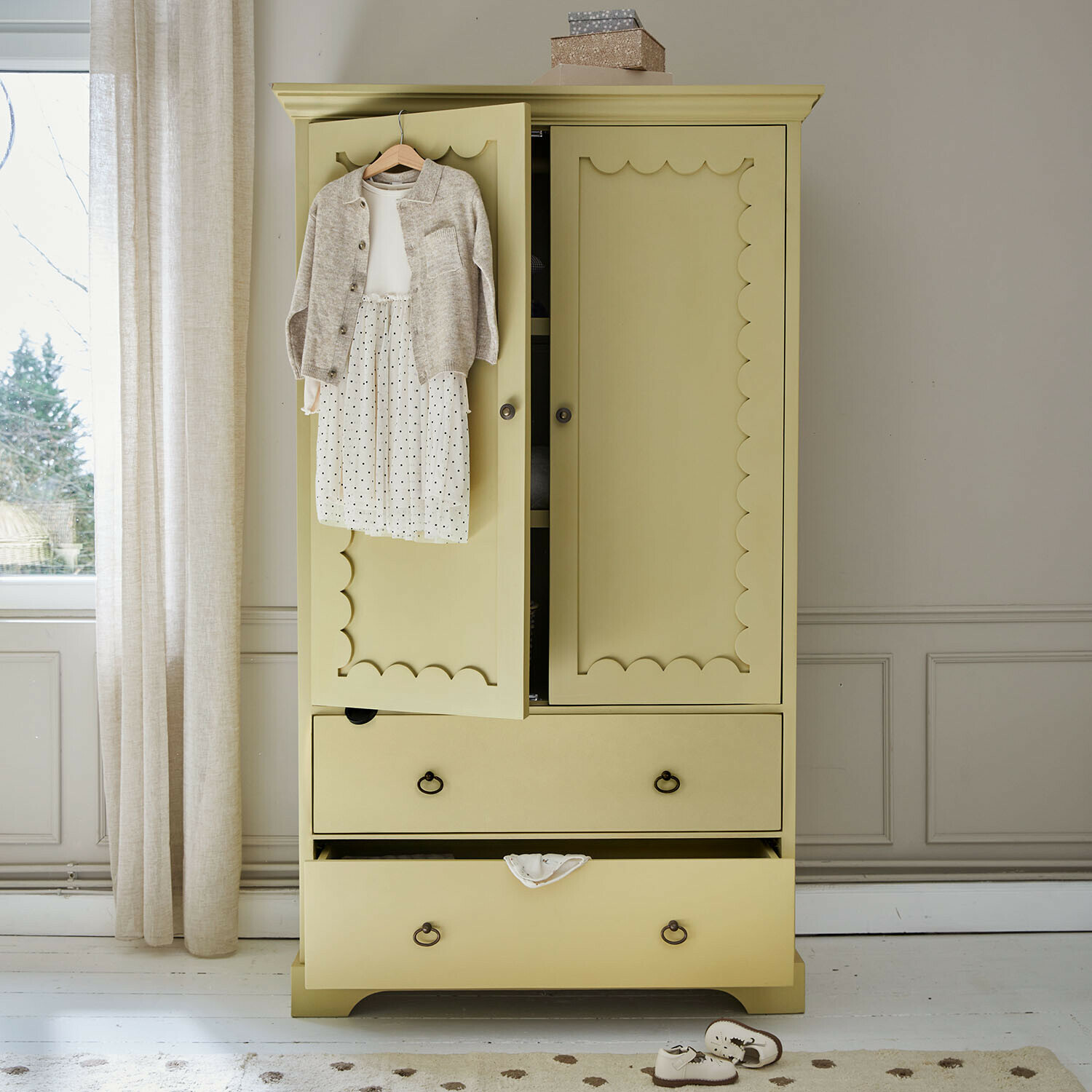 Armario ropero infantil Frollin Armario de madera amarillo con puertas decorativas y ropa infantil colgada en una habitación luminosa