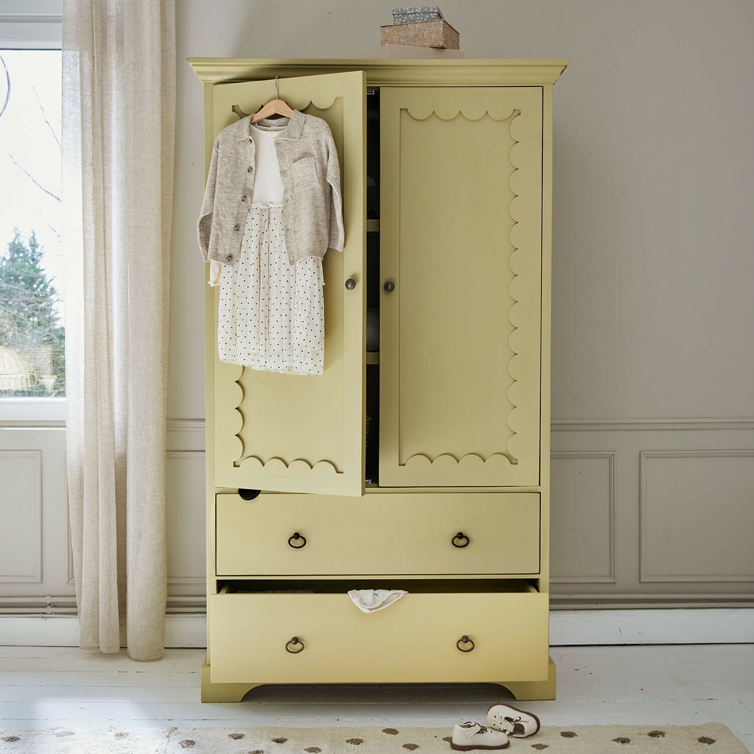 Armario ropero infantil Frollin Armario de madera amarillo con puertas decorativas y ropa infantil colgada en una habitación luminosa