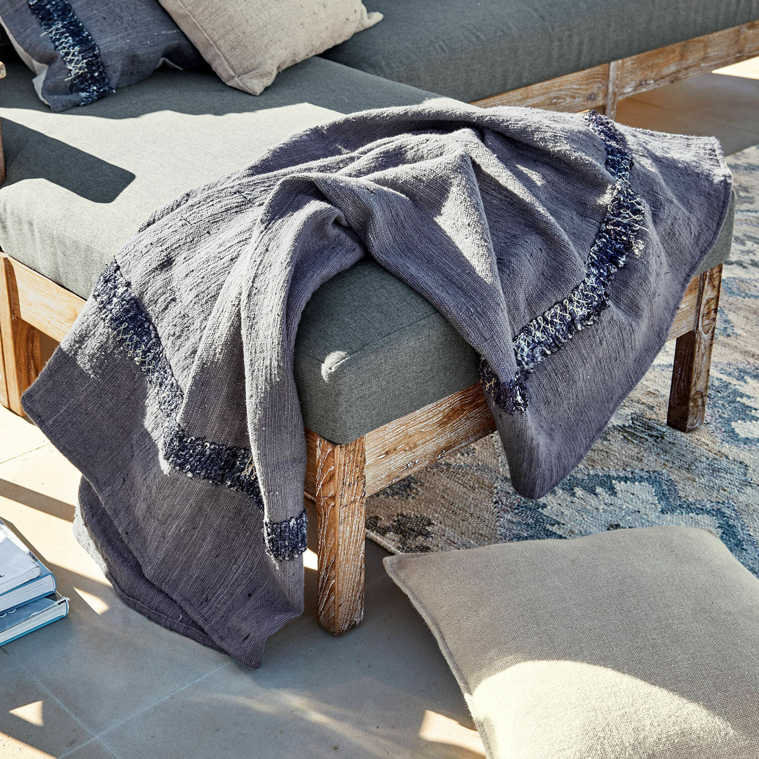 Manta Foix Manta gris de algodón con diseño azul marino sobre banco de madera y cojín beige