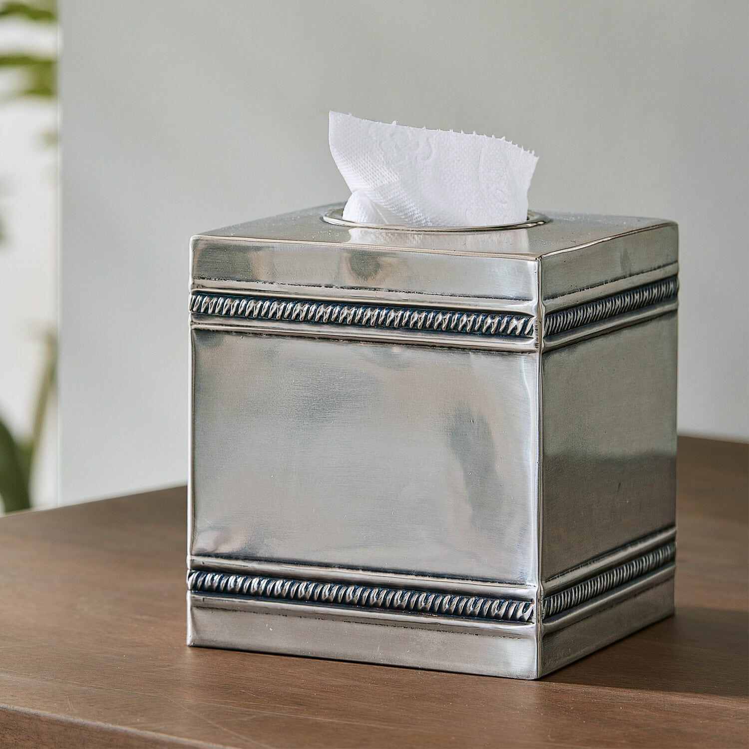 Caja de pañuelos Semoine Dispensador de pañuelos metálico plateado con diseño decorativo en los bordes sobre mesa de madera