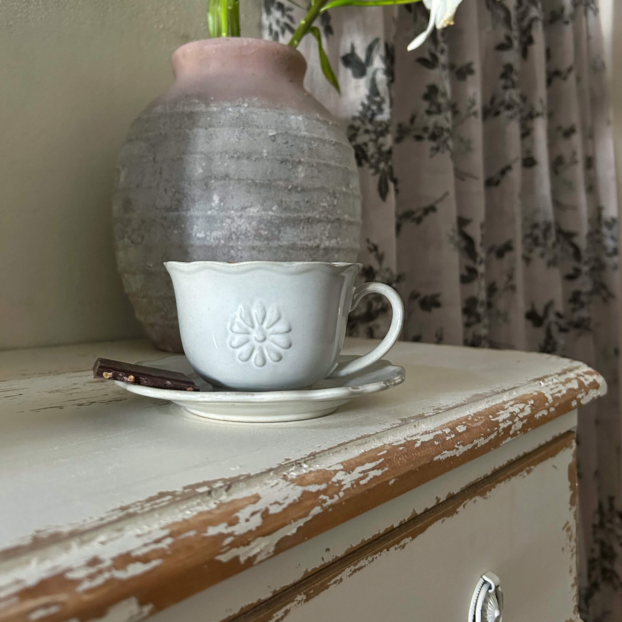 Taza de cerámica blanca con plato y trozo de chocolate sobre mesa de madera envejecida