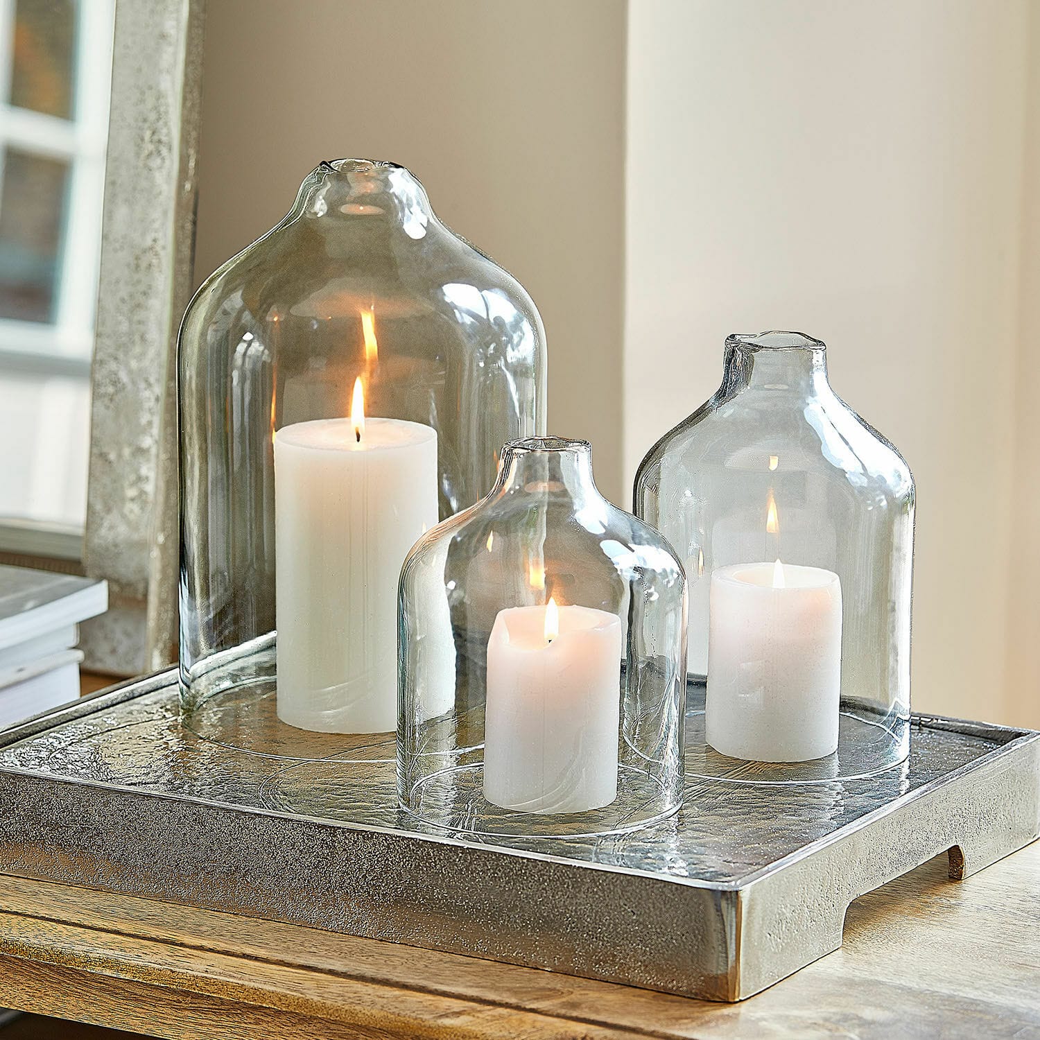 Set de 3 portavelas Xalvent Conjunto de tres campanas de vidrio transparentes con velas blancas sobre bandeja metálica decorativa