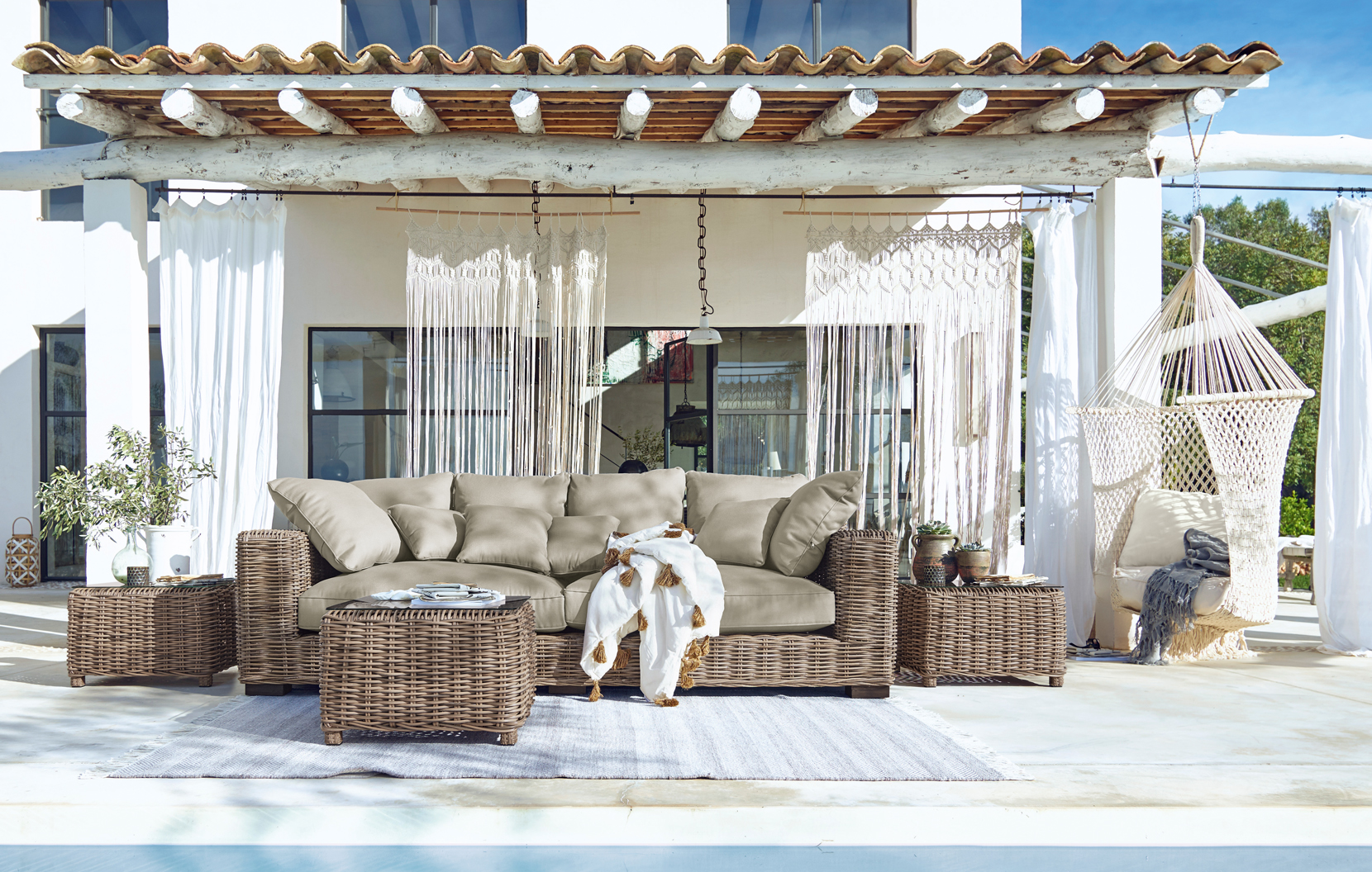 Conjunto de muebles de jardín de mimbre con cojines beige en terraza con hamaca y decoración bohemia