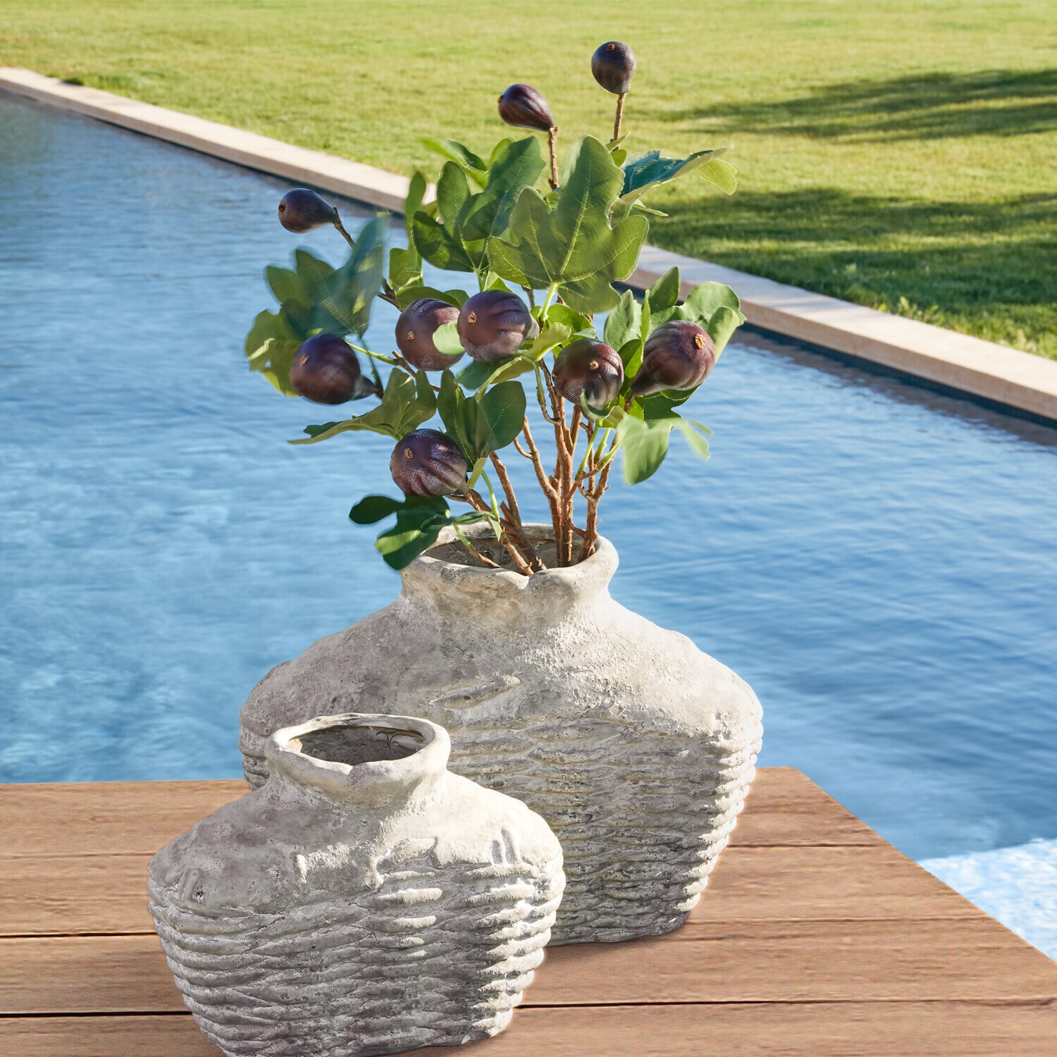 Set de 3 ramas decorativas Alverino Dos jarrones rústicos de cerámica gris sobre mesa de madera junto a piscina con hojas verdes y frutos