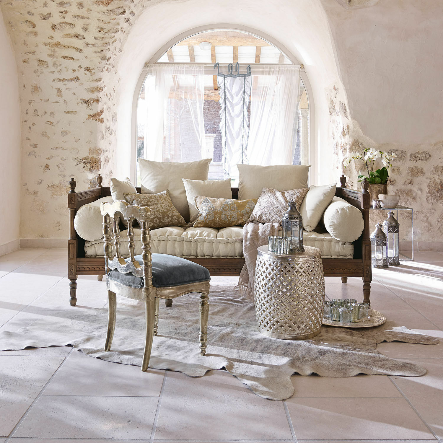 Sofá Douville Sala acogedora con sofá de madera, cojines crema, mesa plateada y silla azul de terciopelo