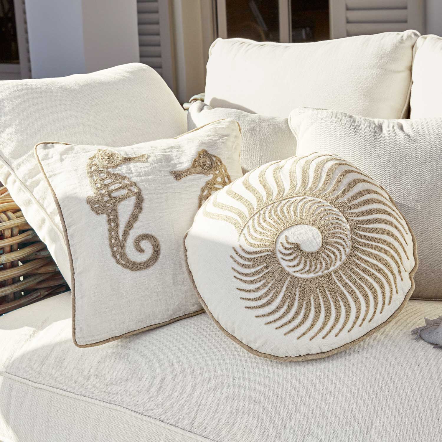 Cojines decorativos beige con motivos de caballitos de mar y concha en sofá claro, textiles para el hogar