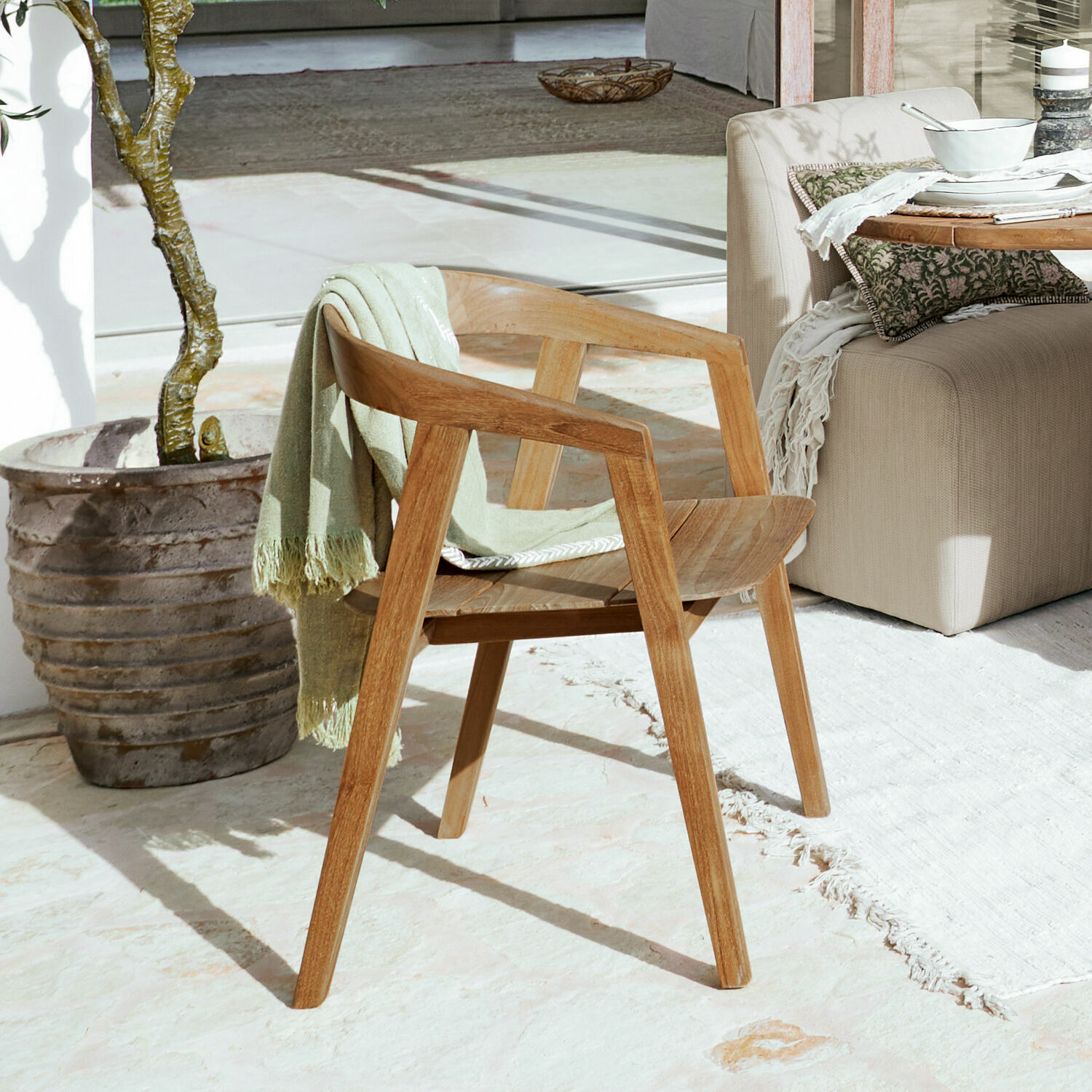 Silla de madera natural con reposabrazos y manta verde en terraza soleada