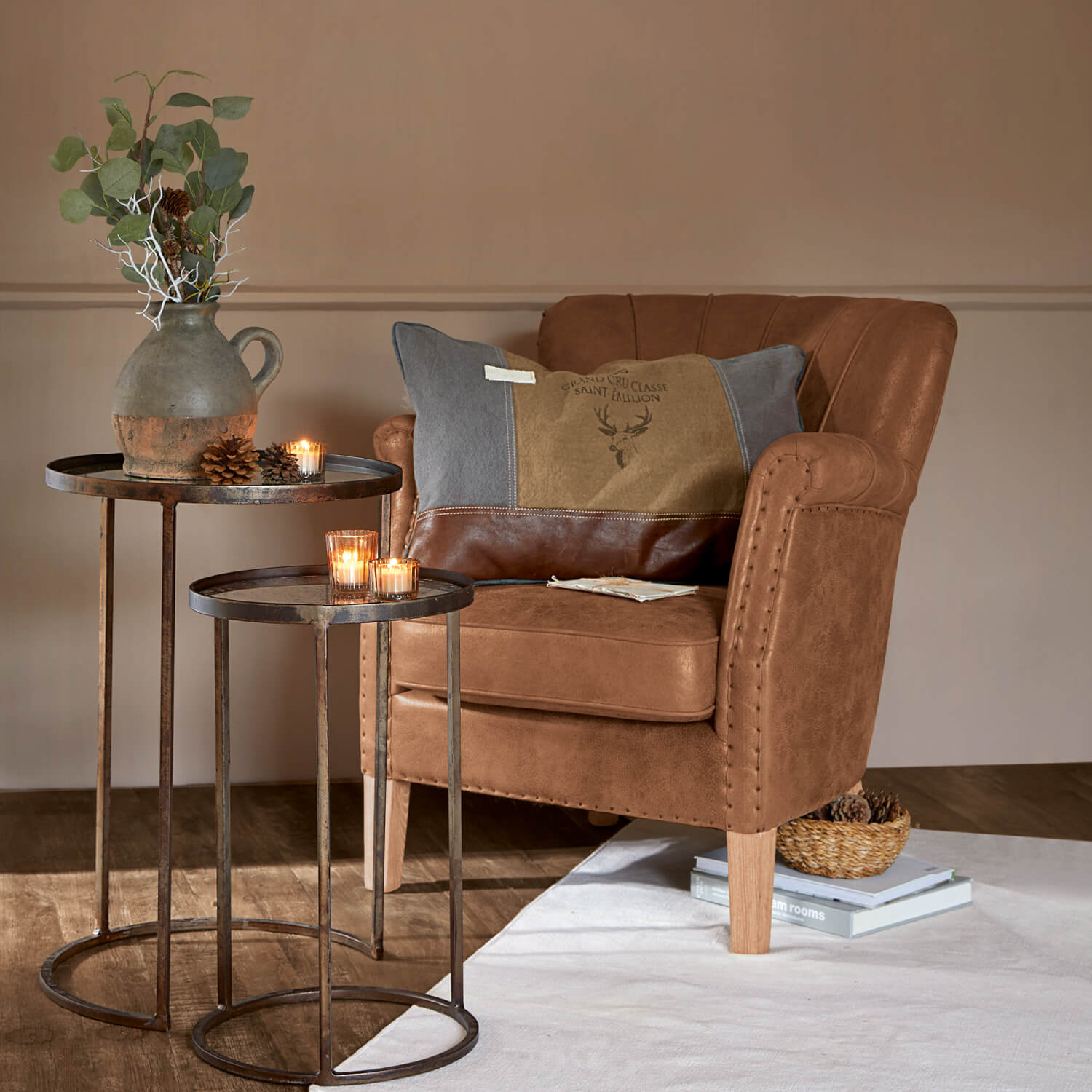Sillón marrón de piel sintética con cojín decorativo y mesas metálicas con velas y jarrón