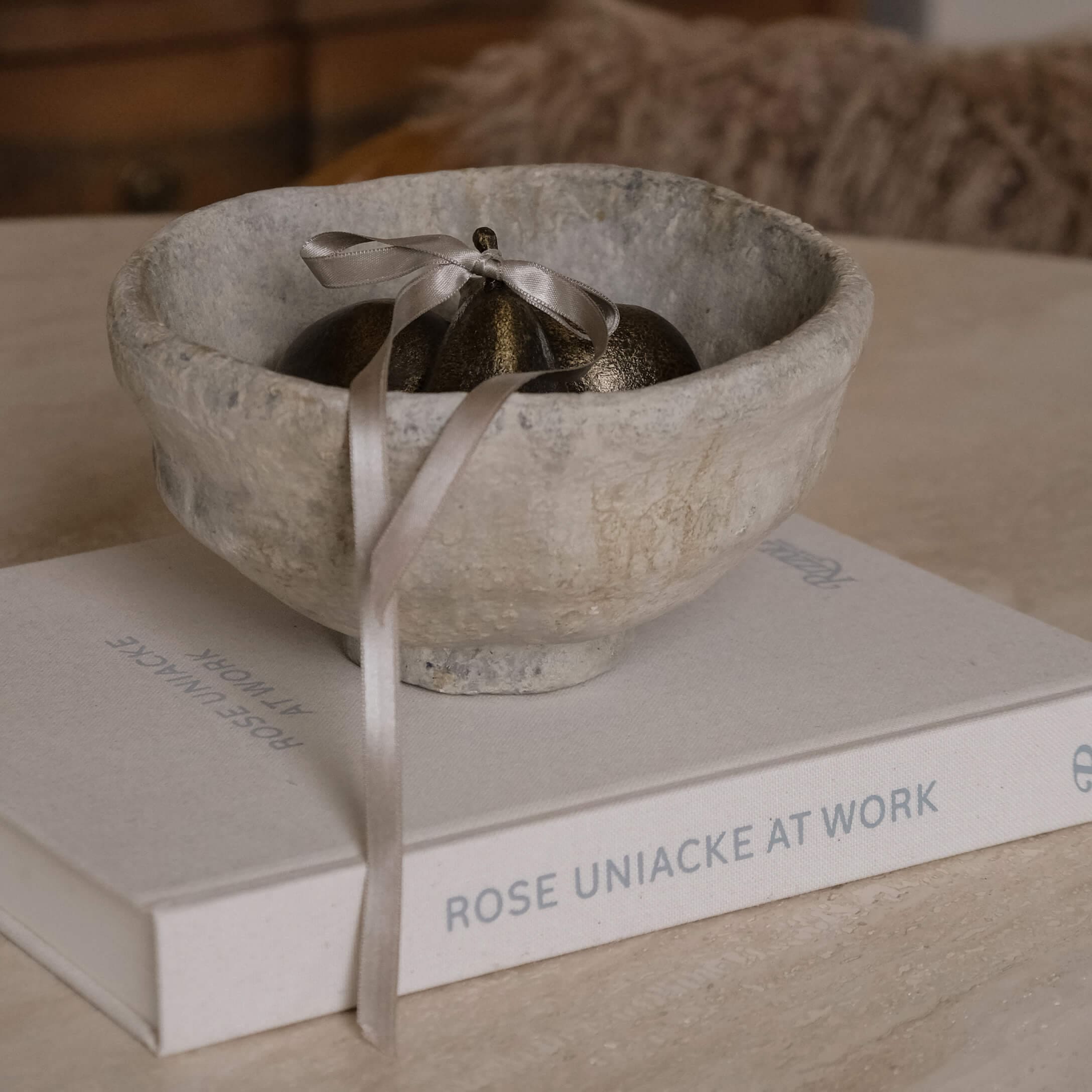 Cuenco decorativo de piedra gris con adorno metálico y lazo sobre un libro en una mesa