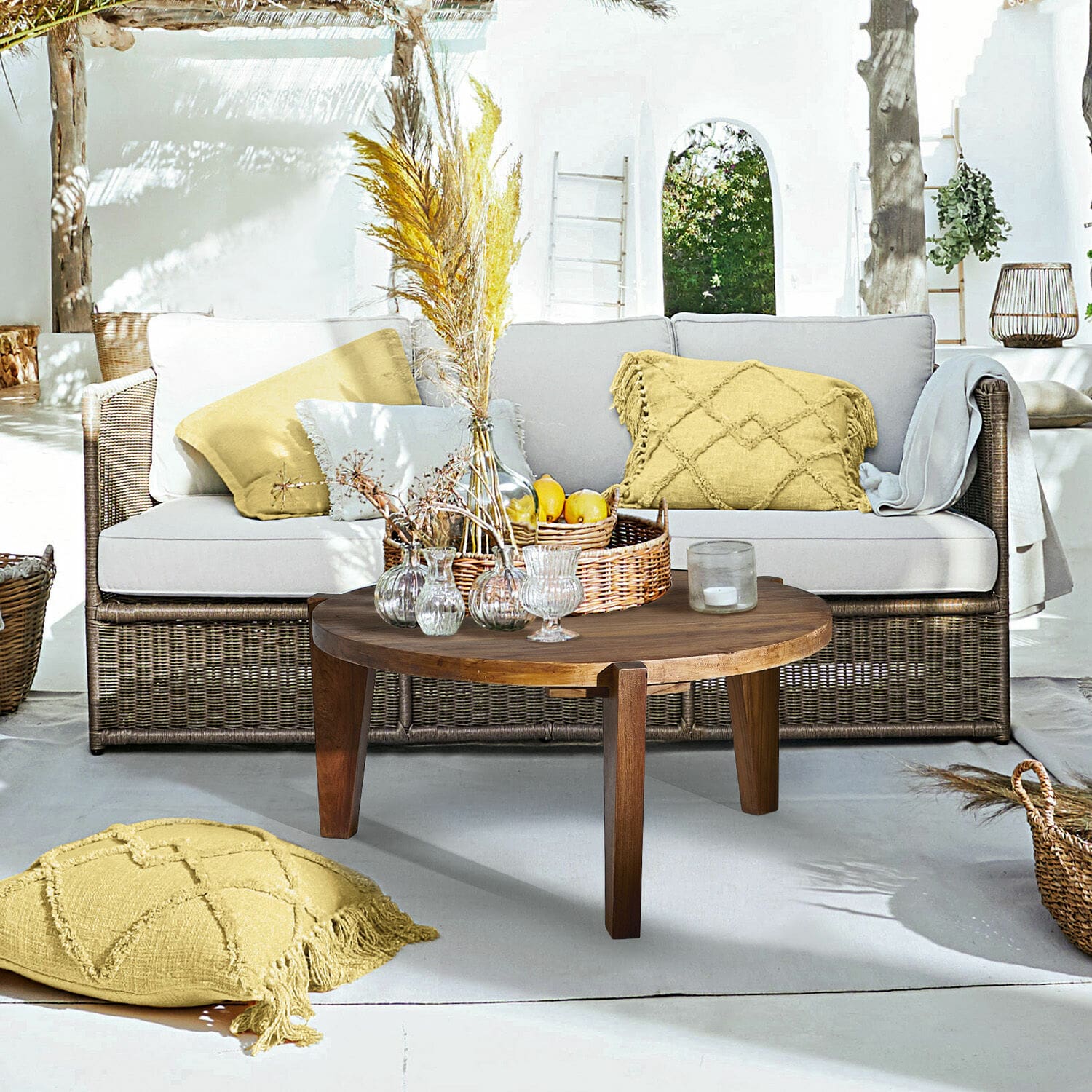 Sofá Lesmont Sala con sofá de mimbre, cojines gris claro y mesa de centro redonda de madera en terraza soleada