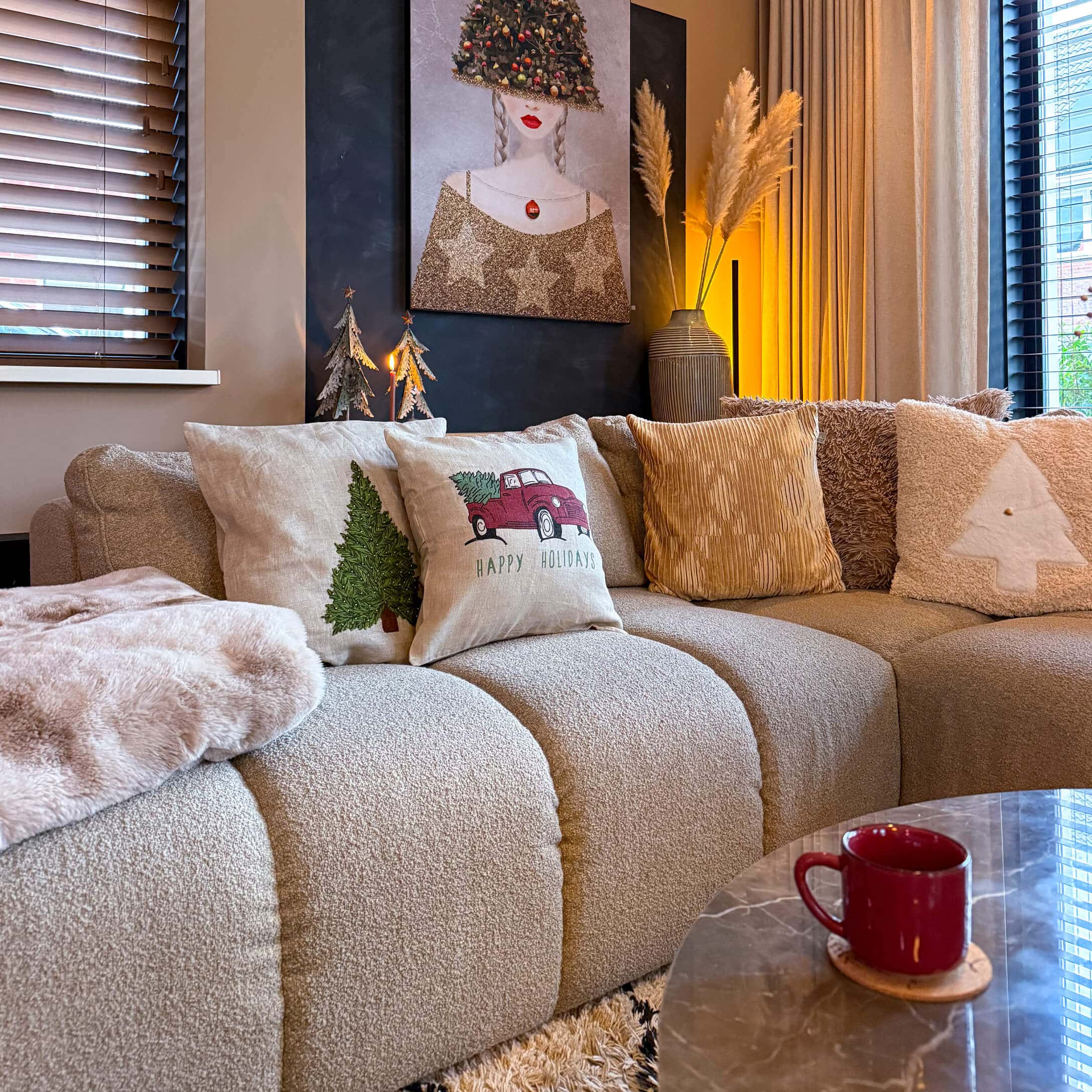 Sofá beige con cojines navideños y taza roja sobre mesa de mármol en sala acogedora