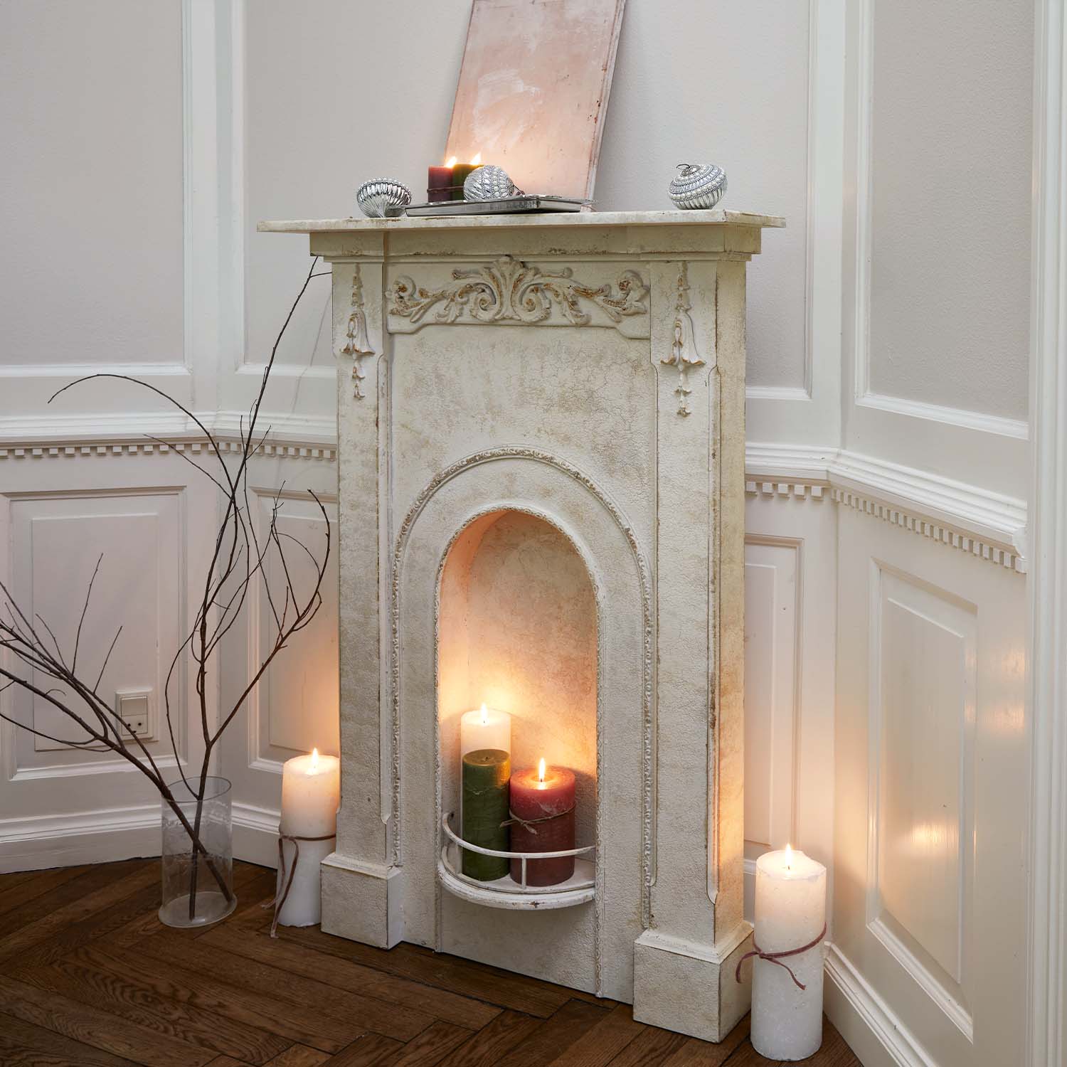 Chimenea decorativa blanca con relieves ornamentales y velas encendidas en interior rústico