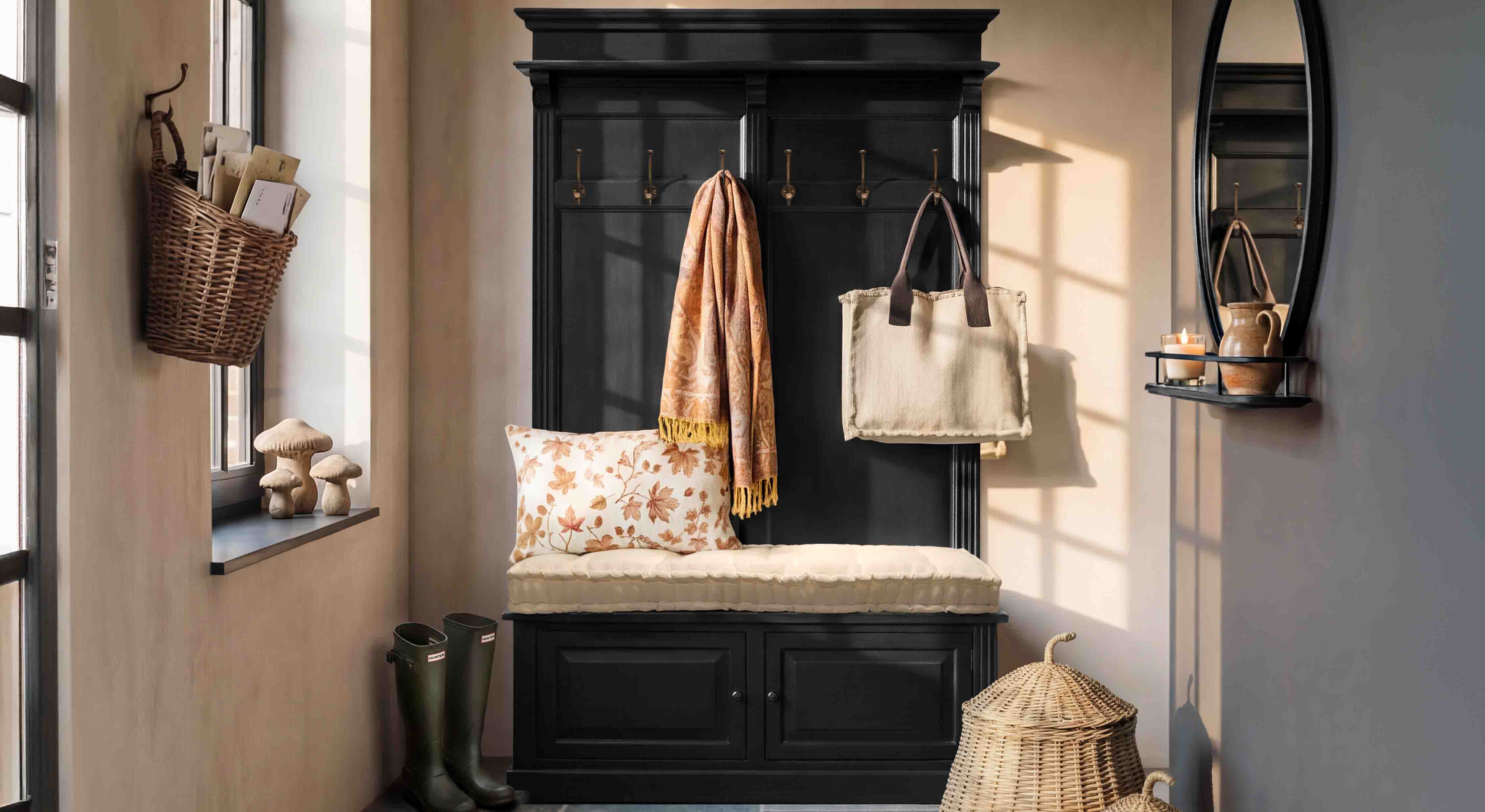 Mueble negro de madera con asiento acolchado, cojín y ganchos de pared en un recibidor acogedor