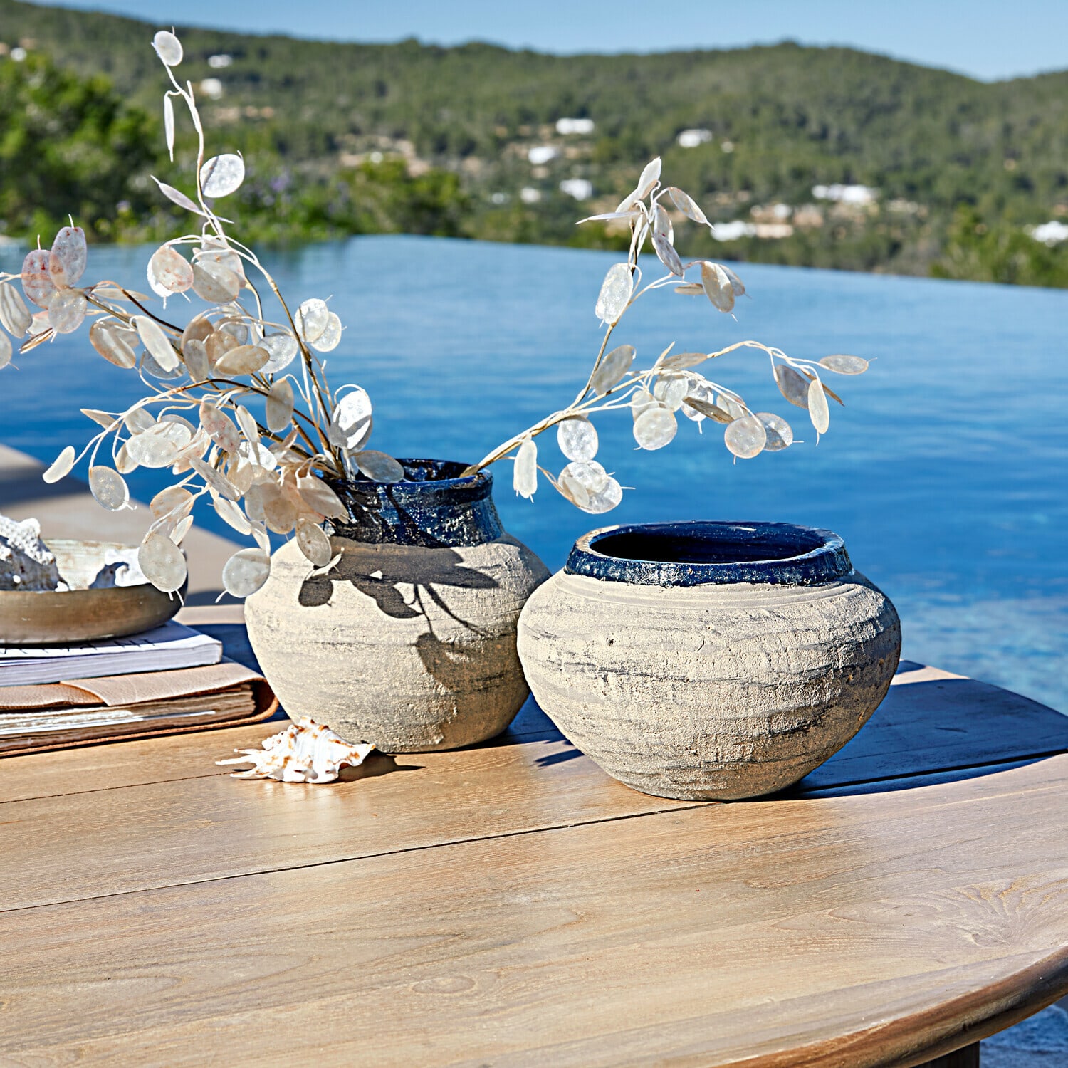 Set de 2 jarrones Dolciaro Dos jarrones de cerámica beige con borde azul sobre mesa de madera junto a piscina