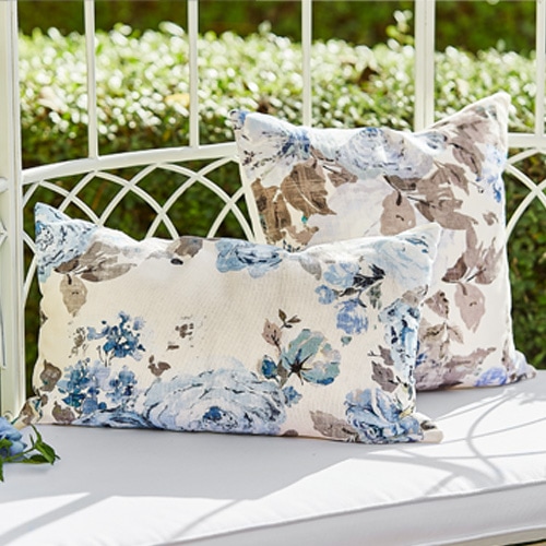 Cojines decorativos con estampado floral azul y beige sobre banco de jardín blanco de metal