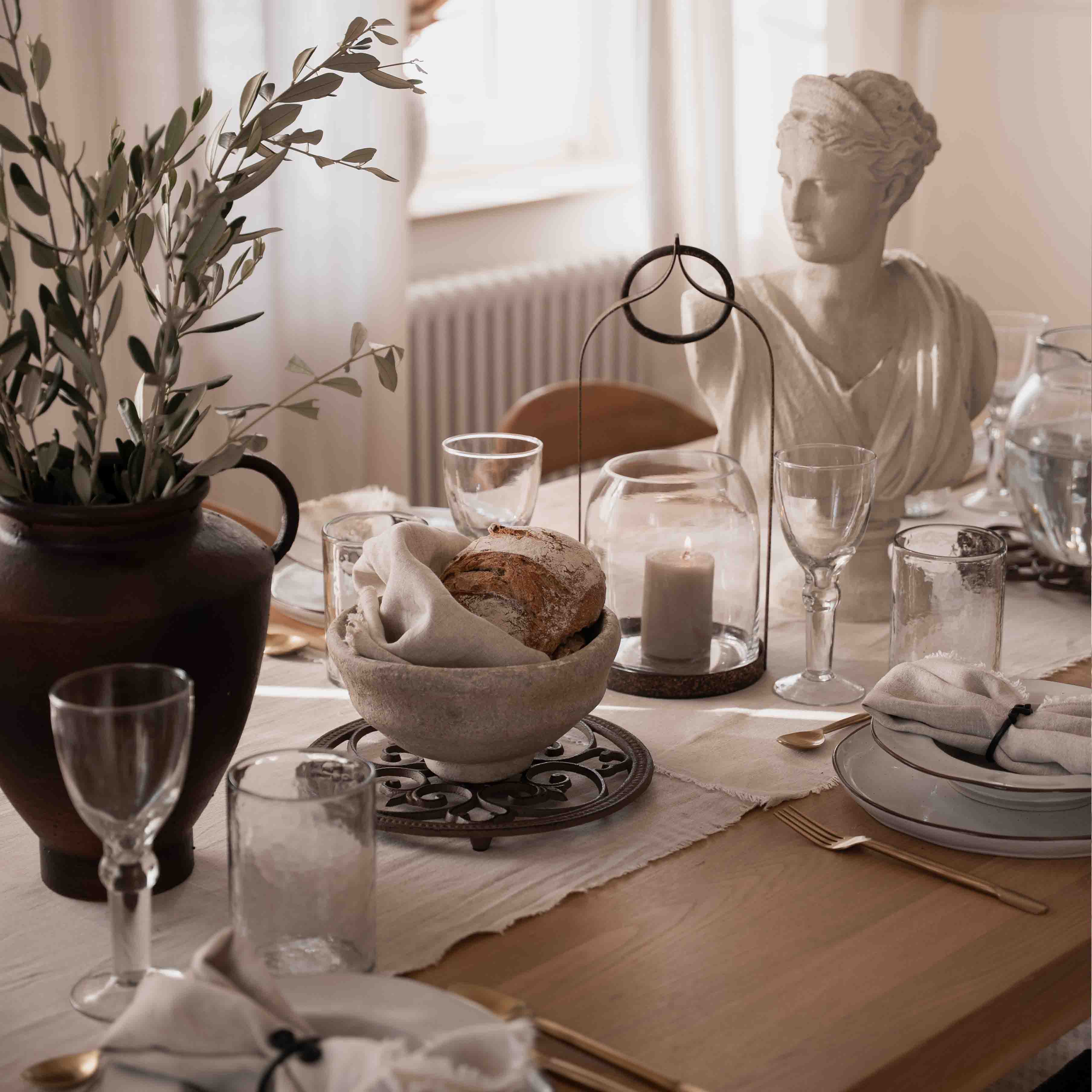 Decoración de mesa sobria con pan, vela y estatua de piedra blanca a la luz natural