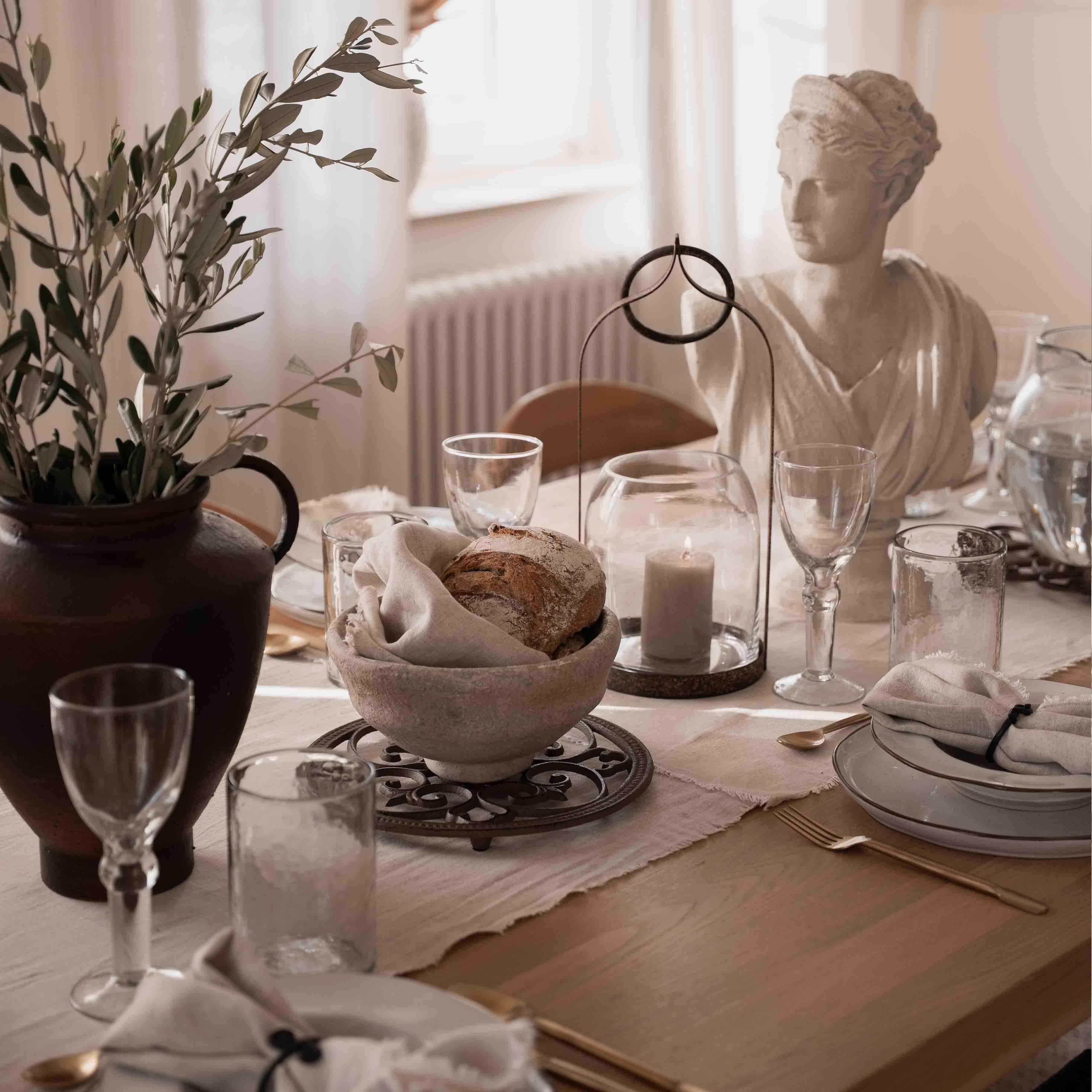 Decoración de mesa sobria con pan, vela y estatua de piedra blanca a la luz natural