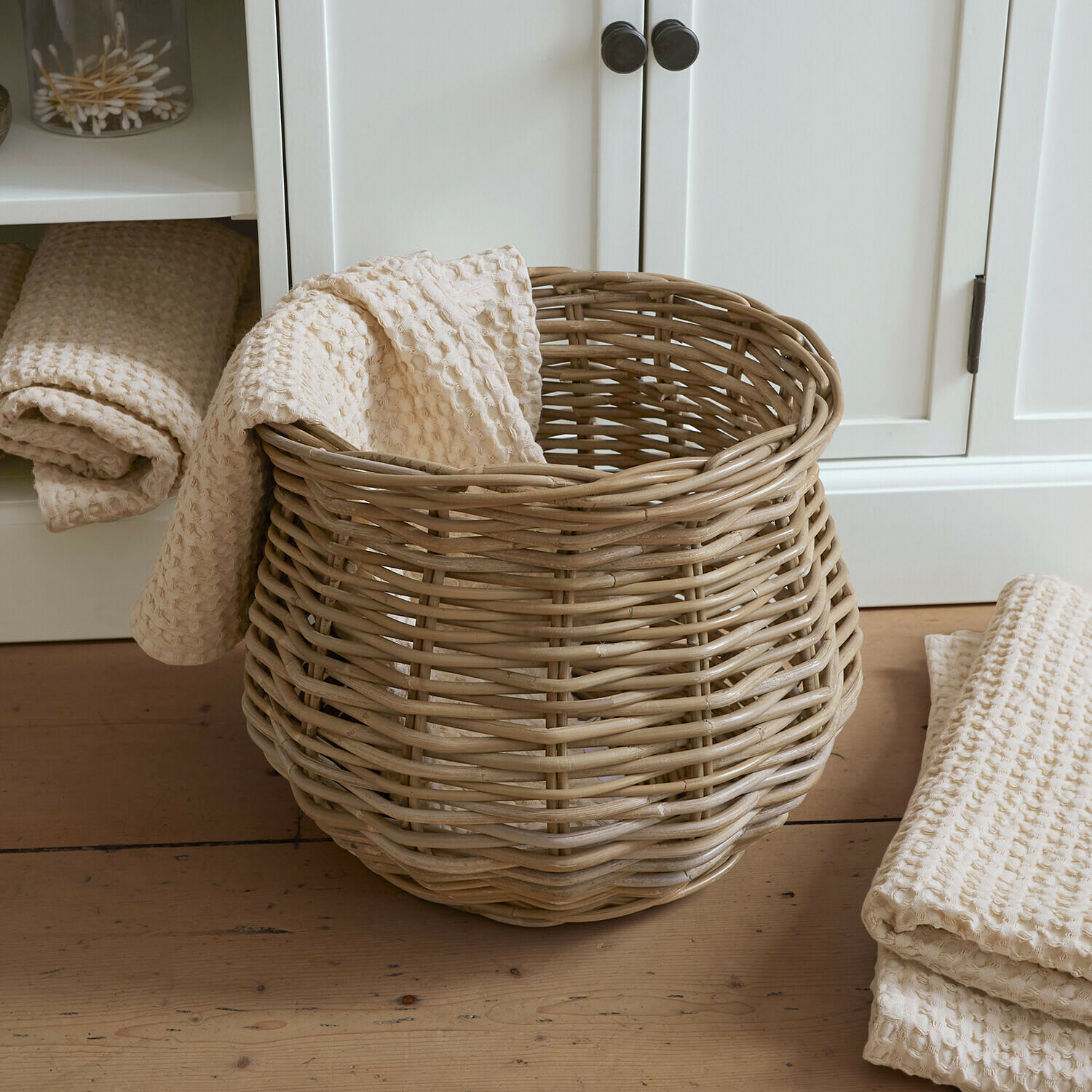 Cesta Elvendia Cesta de mimbre natural con toalla crema de textura gofrada sobre suelo de madera clara