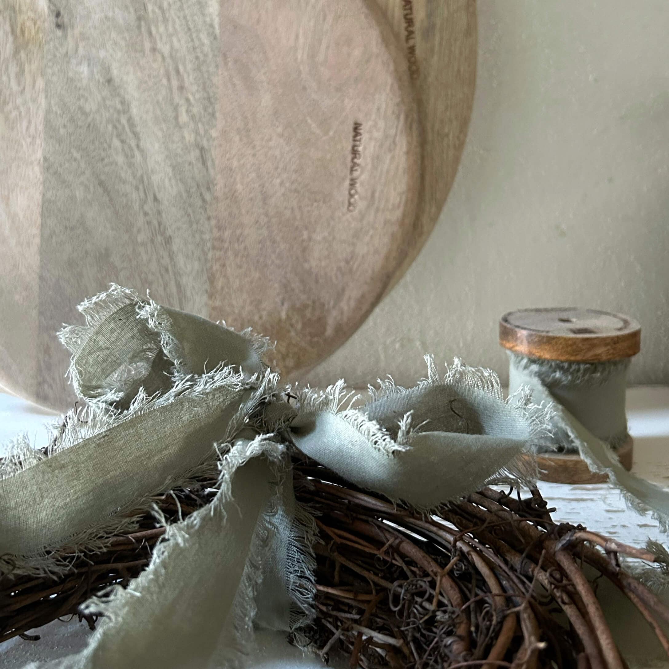 Plato de madera natural con cinta de lino gris sobre corona de mimbre para decoración interior