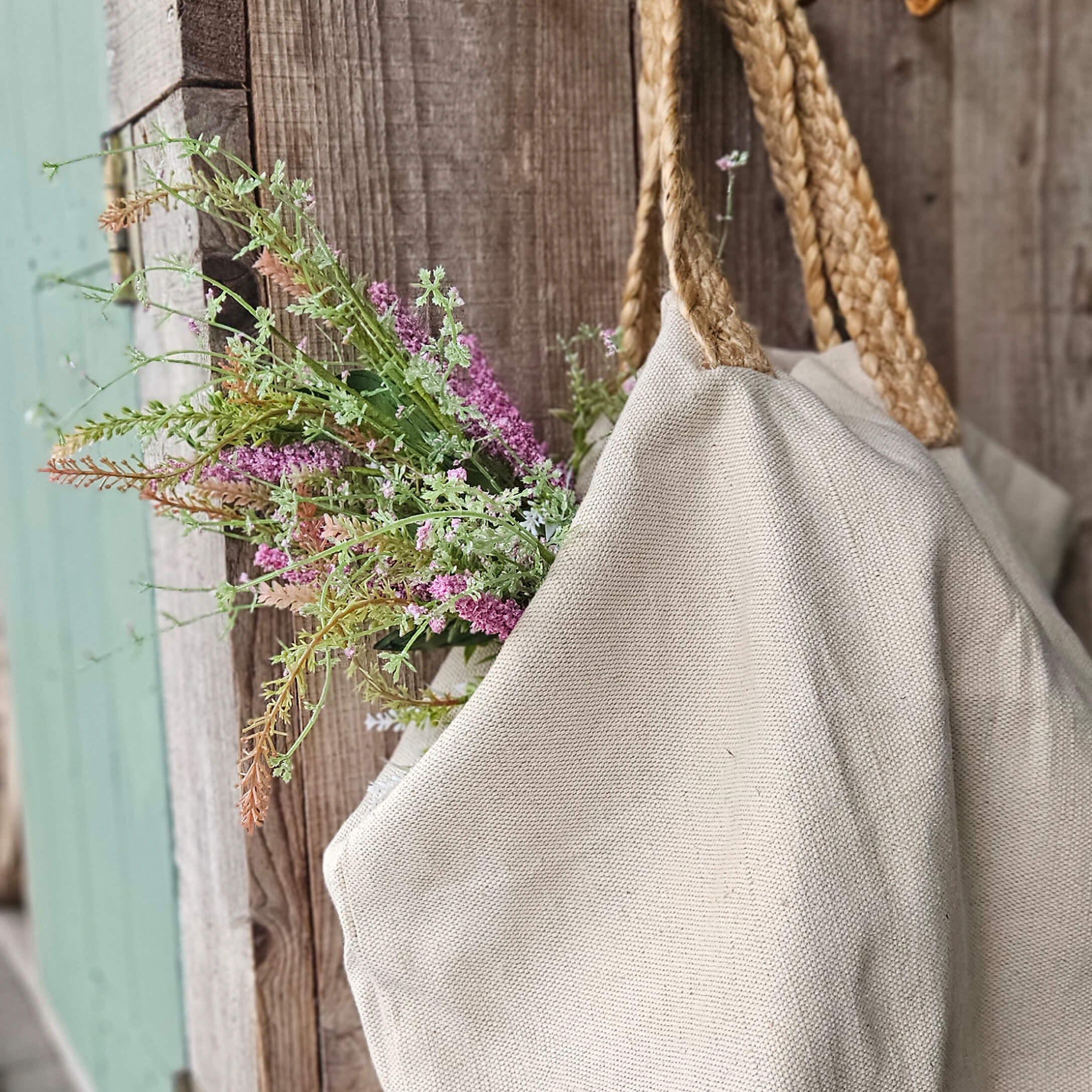 Bolsa beige de material natural con asas trenzadas y flores sobre fondo de madera rústica