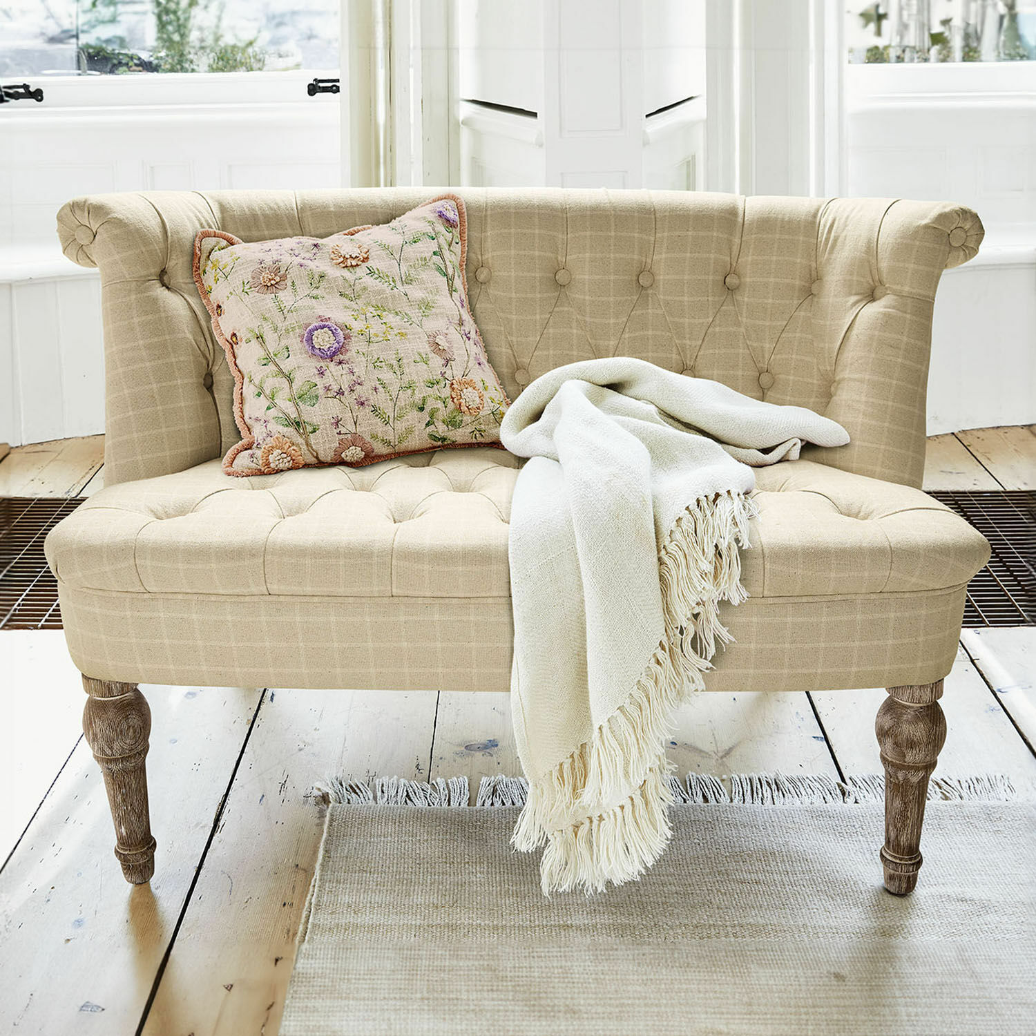 Sofá Weralin Sofá tapizado beige con patas de madera, cojín decorativo y manta crema sobre alfombra clara