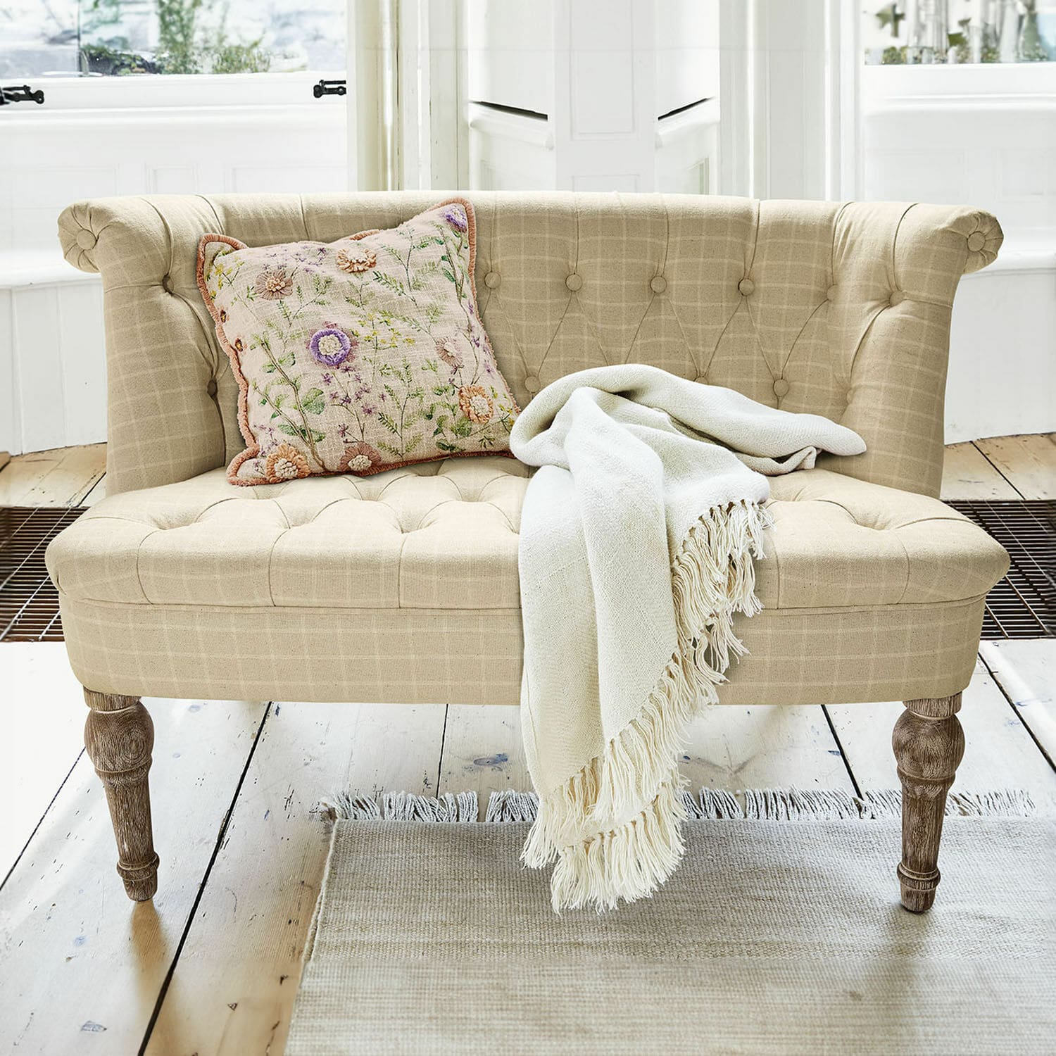 Sofá Weralin Sofá tapizado beige con patas de madera, cojín decorativo y manta crema sobre alfombra clara