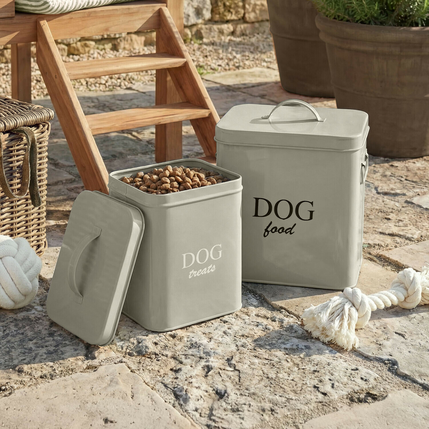 Contenedores metálicos grises para comida y premios de perro sobre suelo de piedra en exterior