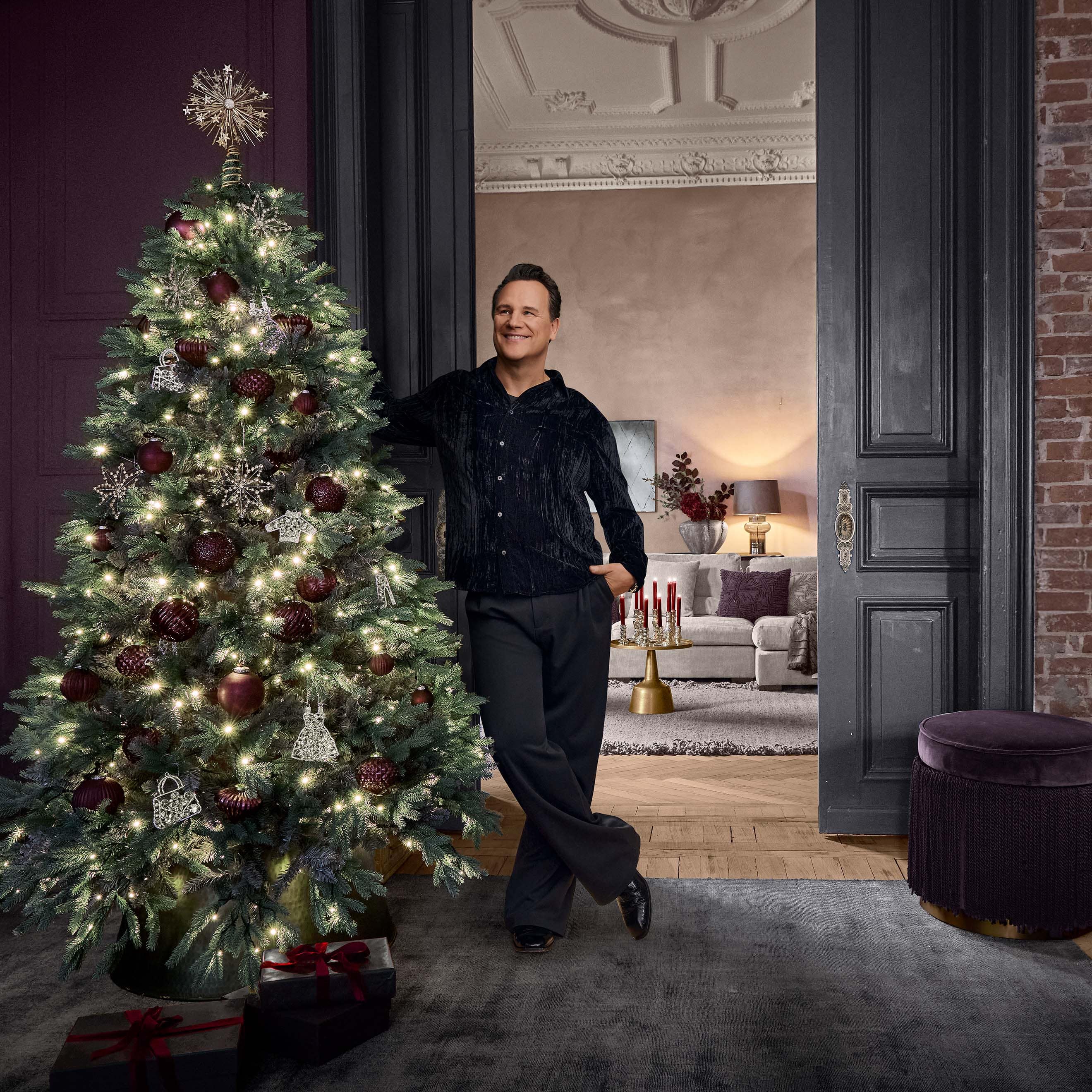 Árbol de Navidad decorado con bolas rojas y adornos plateados con luces en interior elegante con hombre.
