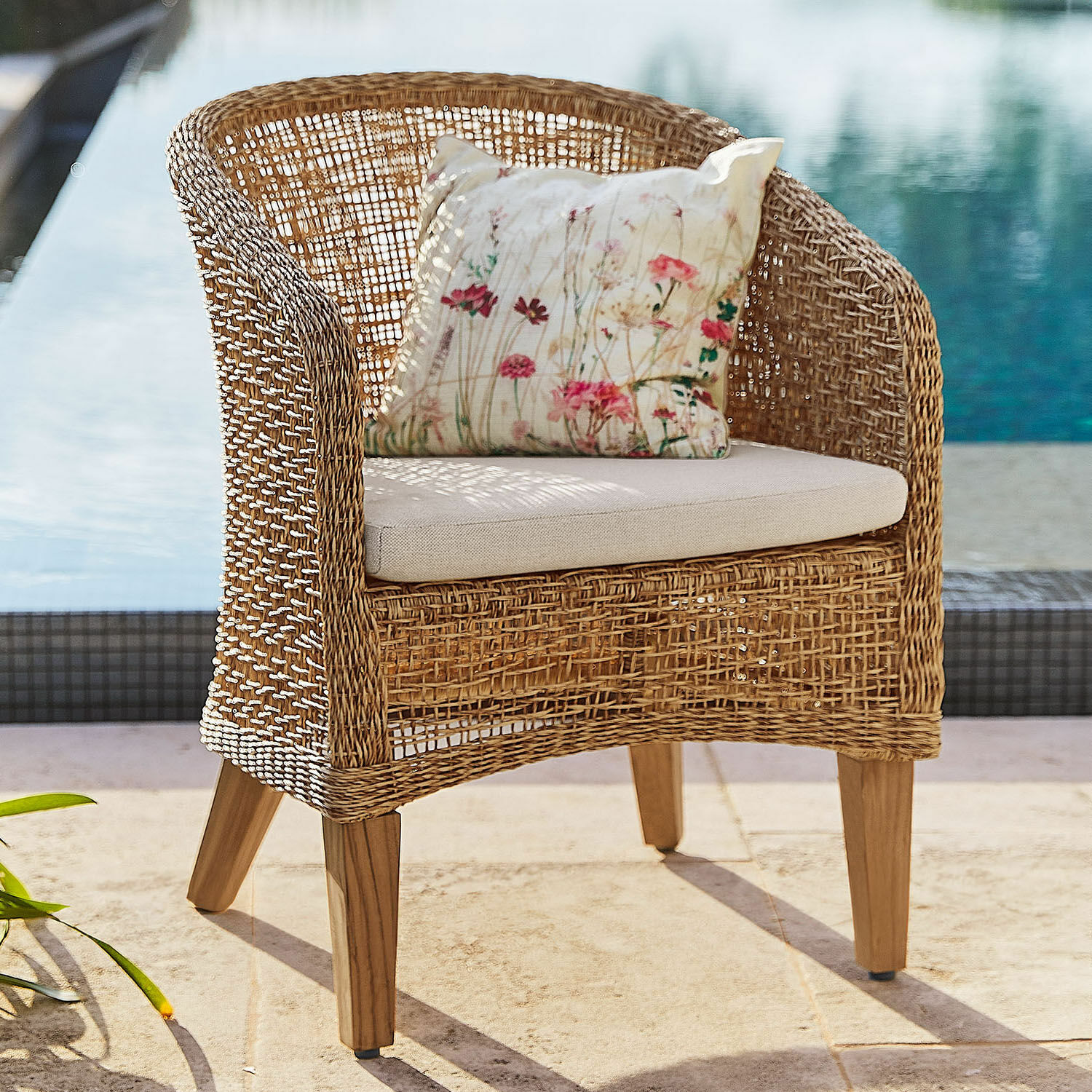 Sillón de ratán con cojín claro y funda floral, ideal para jardín y terraza