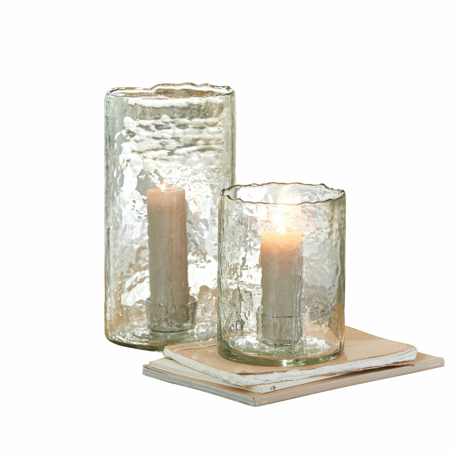 Set de 2 portavelas Querlay Dos portavelas de vidrio transparente con textura y velas blancas sobre una pila de libros