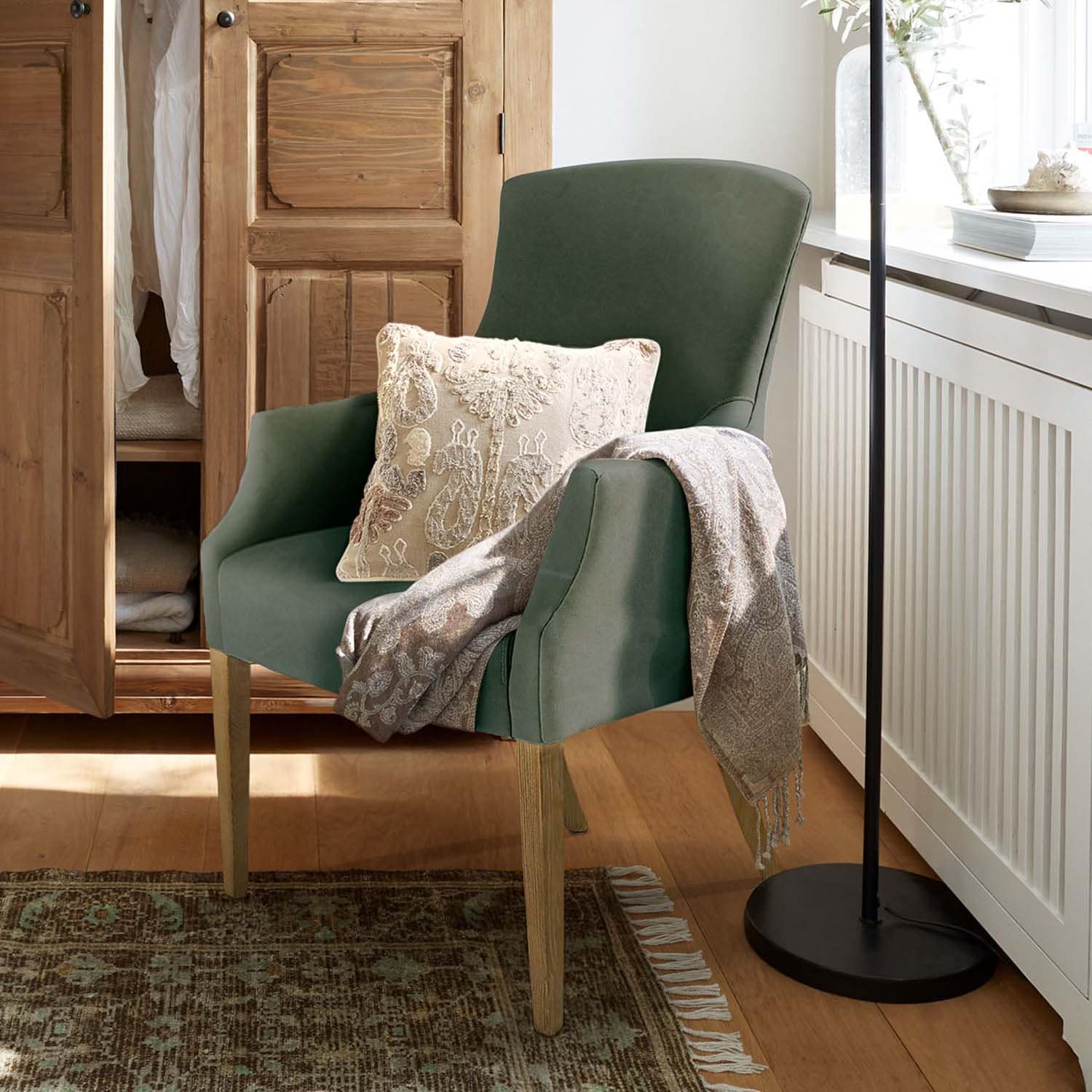 Sillón verde tapizado con patas de madera, cojín decorativo y manta gris en ambiente acogedor