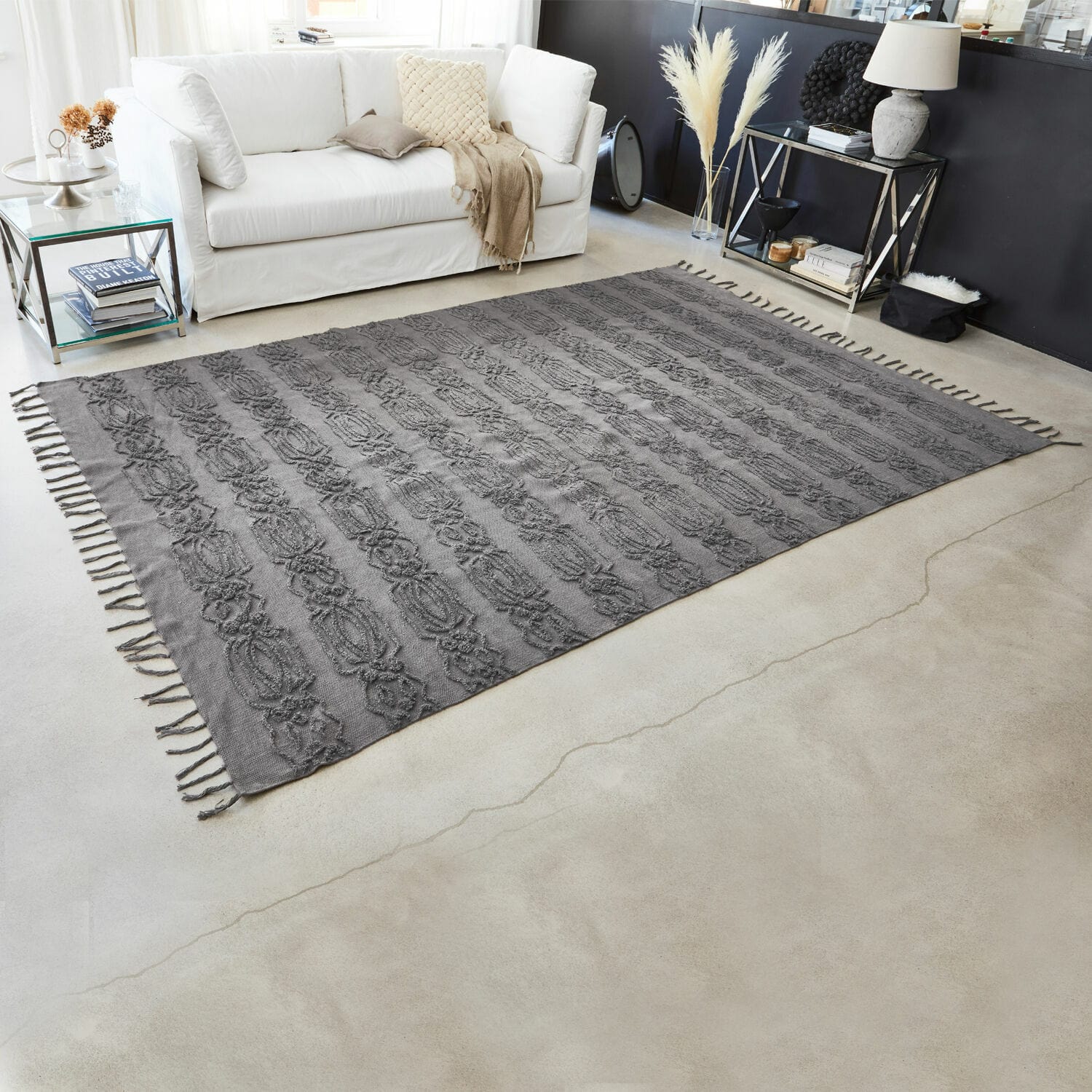Alfombra gris de algodón con diseño decorativo y flecos en sala moderna con sofá blanco