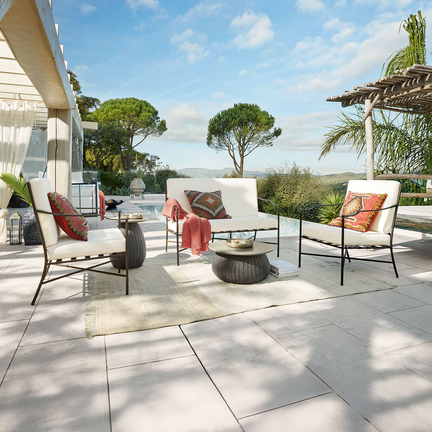 Conjunto de muebles de jardín con estructura metálica y cojines crema en terraza con vista a piscina