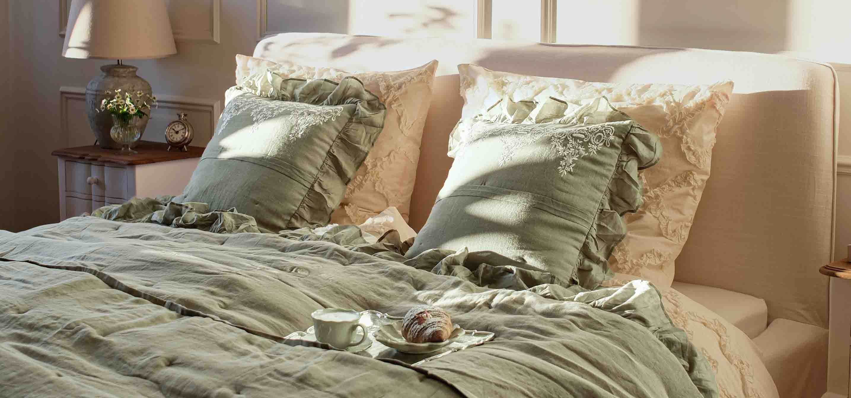 Ropa de cama verde y cojines con volantes en cama de dormitorio luminoso con lámpara y reloj