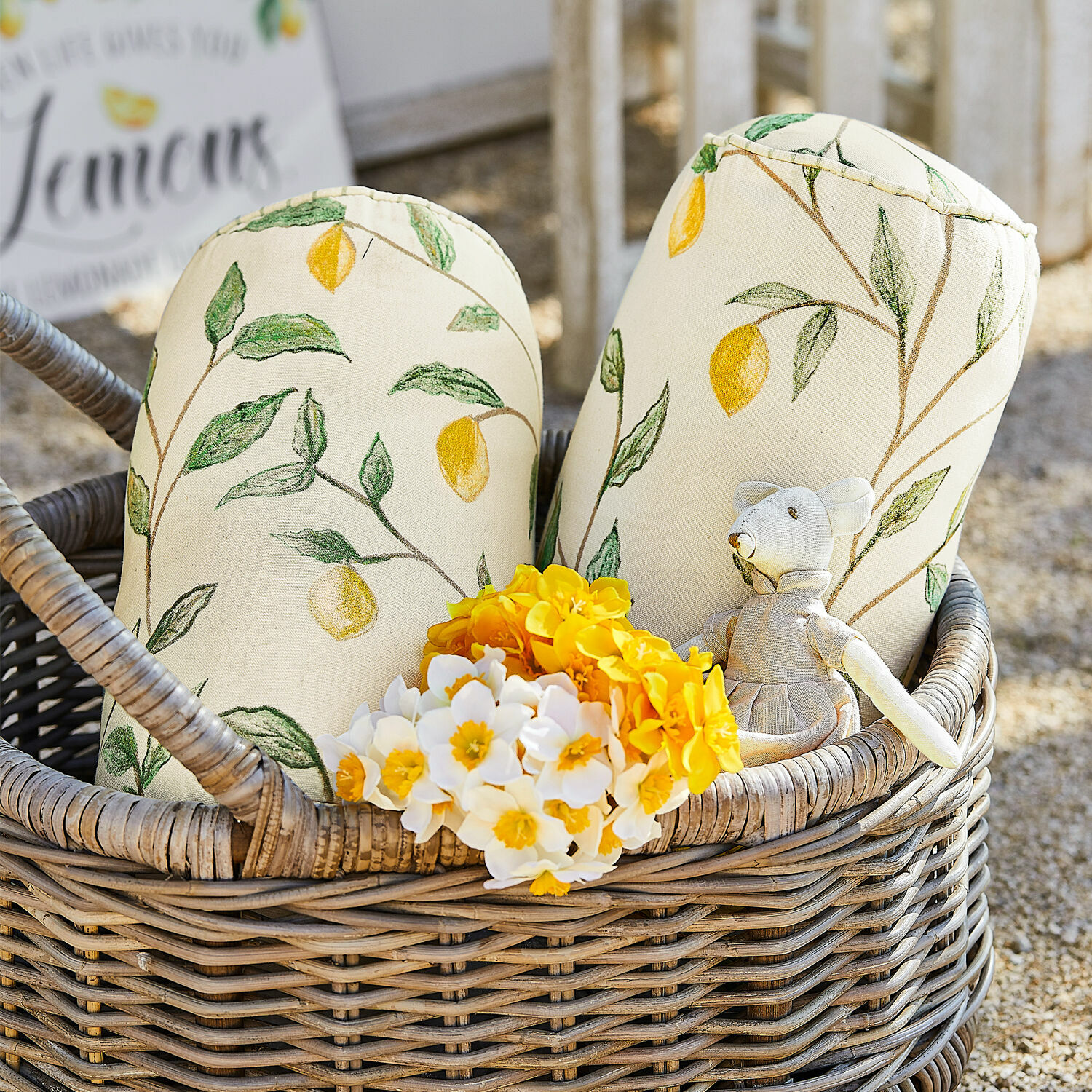 Set de 2 cojines cilíndricos Palerina Cojines decorativos de algodón color crema con estampado de limones en cesta de mimbre con flores