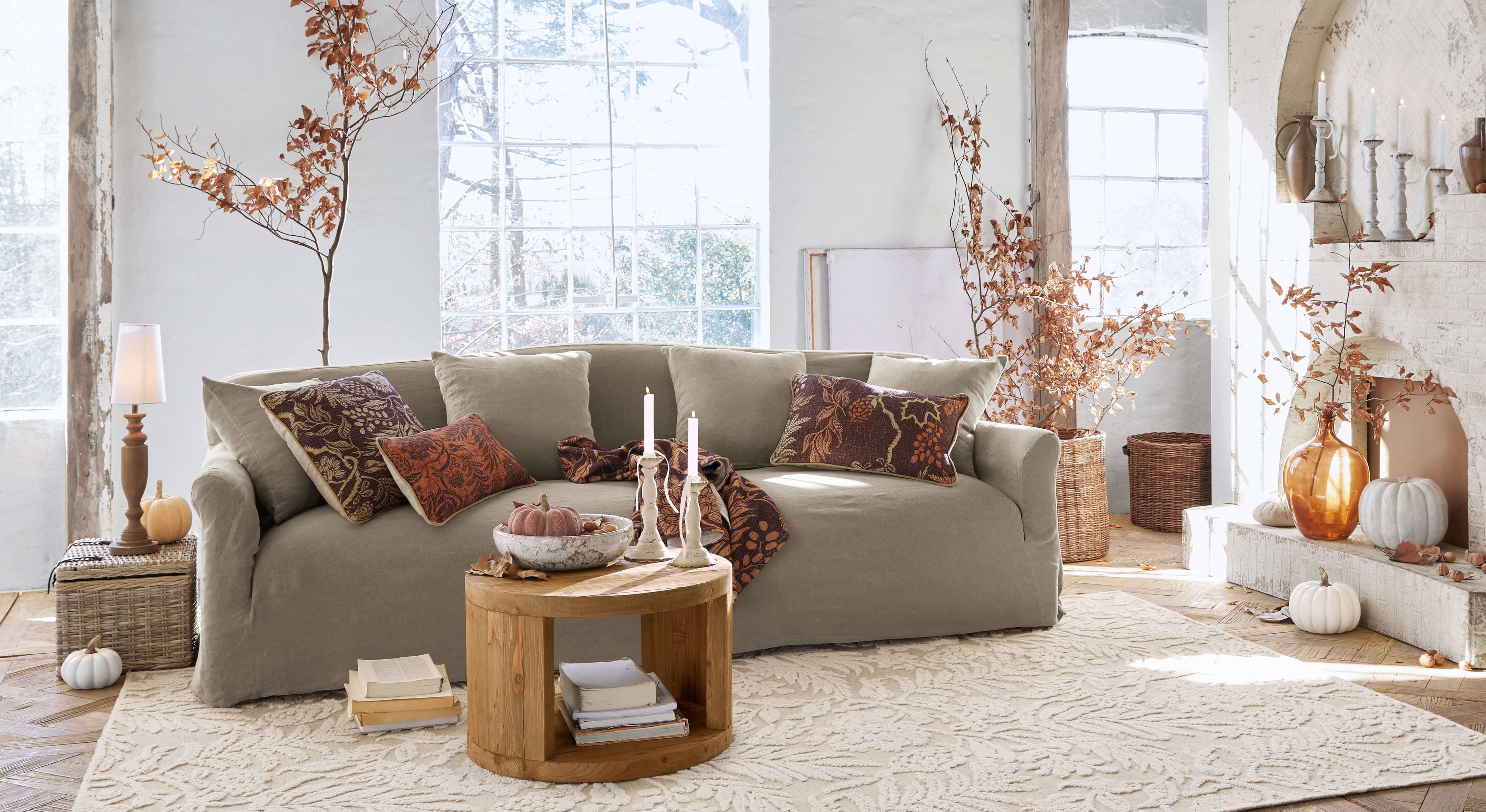 Sofá beige de tela en salón acogedor con decoración otoñal y mesa de centro de madera